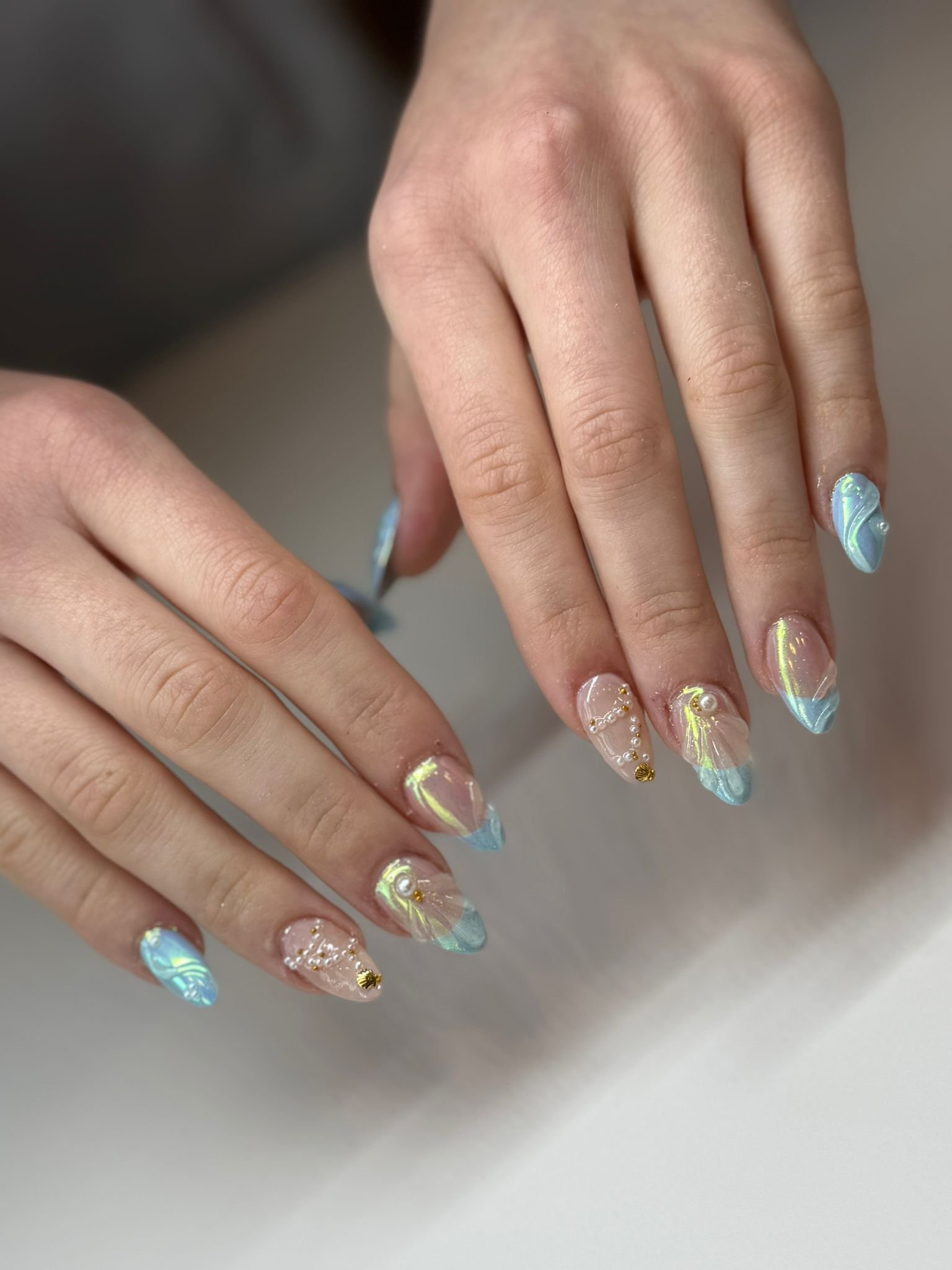 Close-up of hands with decorated fingernails featuring a blue and yellow swirling marble effect and small gold accents.