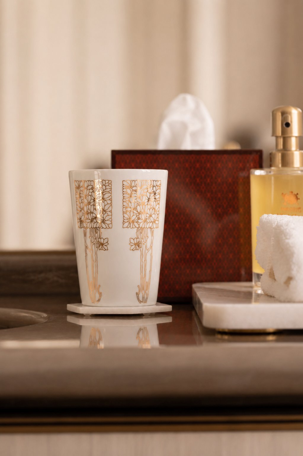 A white ceramic mug with gold floral and tree design, placed on a coaster on a marble surface, with a tissue box and soap dispenser in the background.