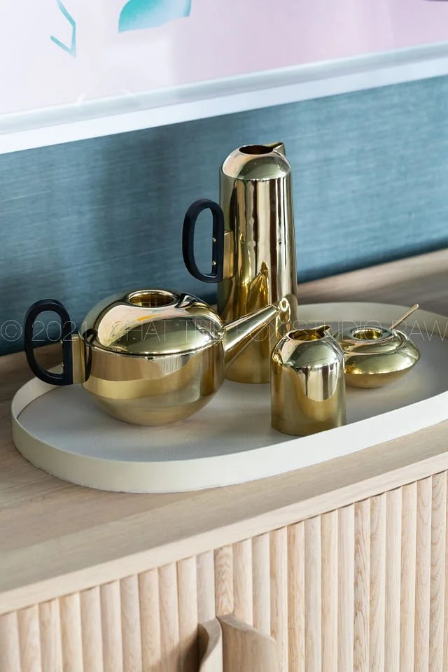 Set of shiny gold teapots and cups with black handles on a white tray.