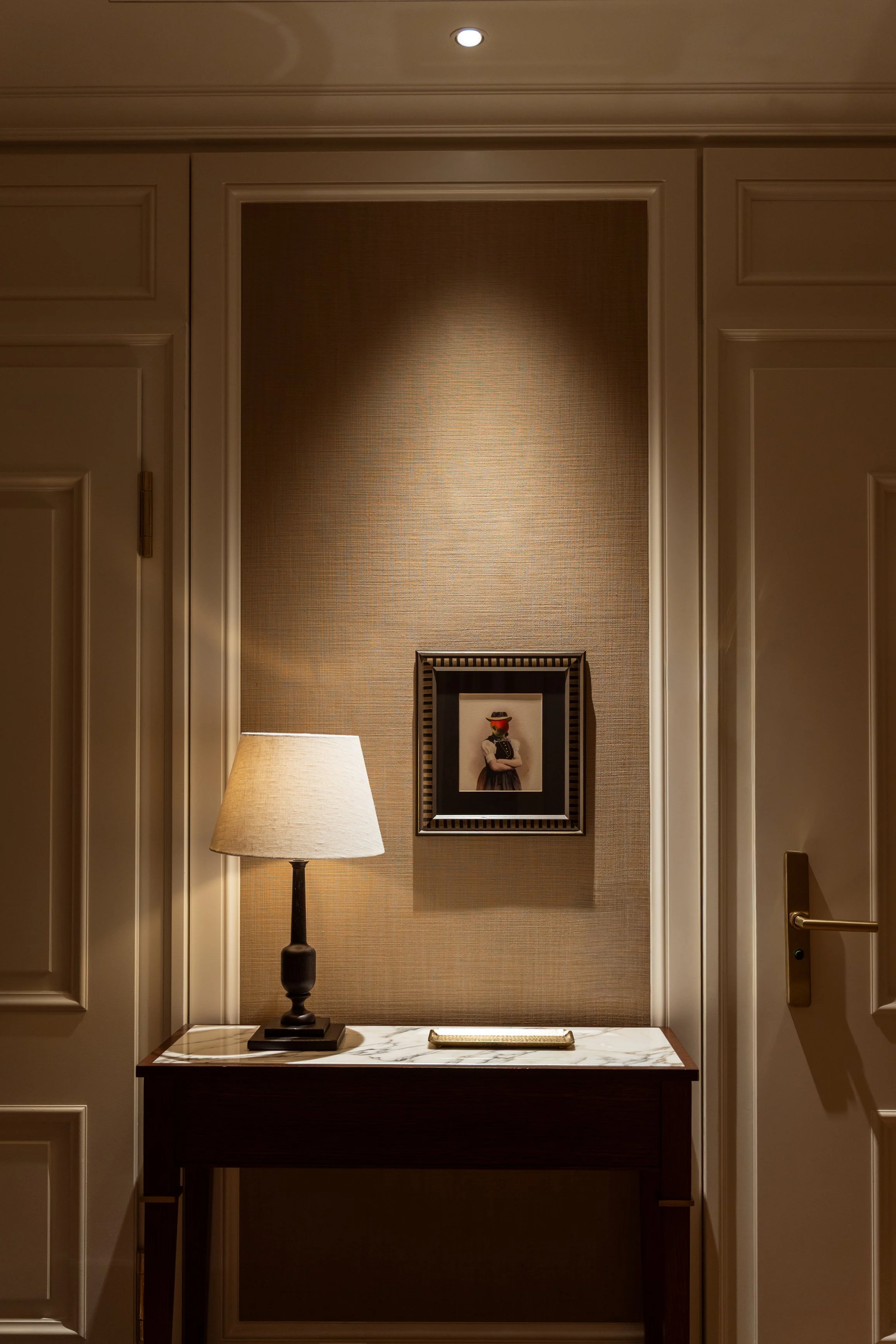 Interior decor with a table, lamp, framed artwork on textured wall, and a door on each side.