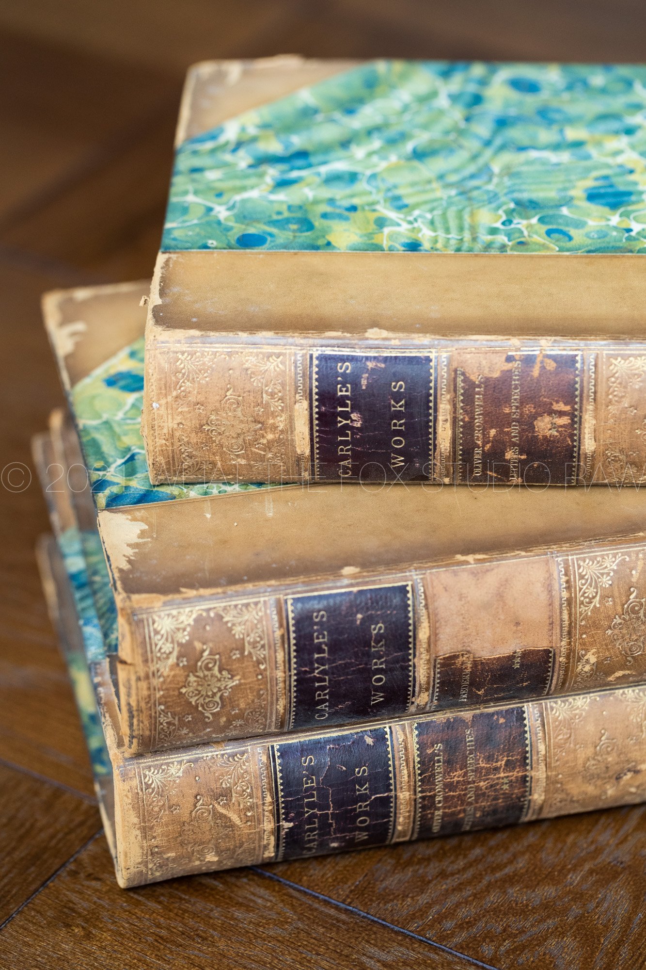 Close-up of a vintage hardcover book titled "Carley's Style & Works," with an ornate gold and blue design on the cover, placed on a wooden surface.