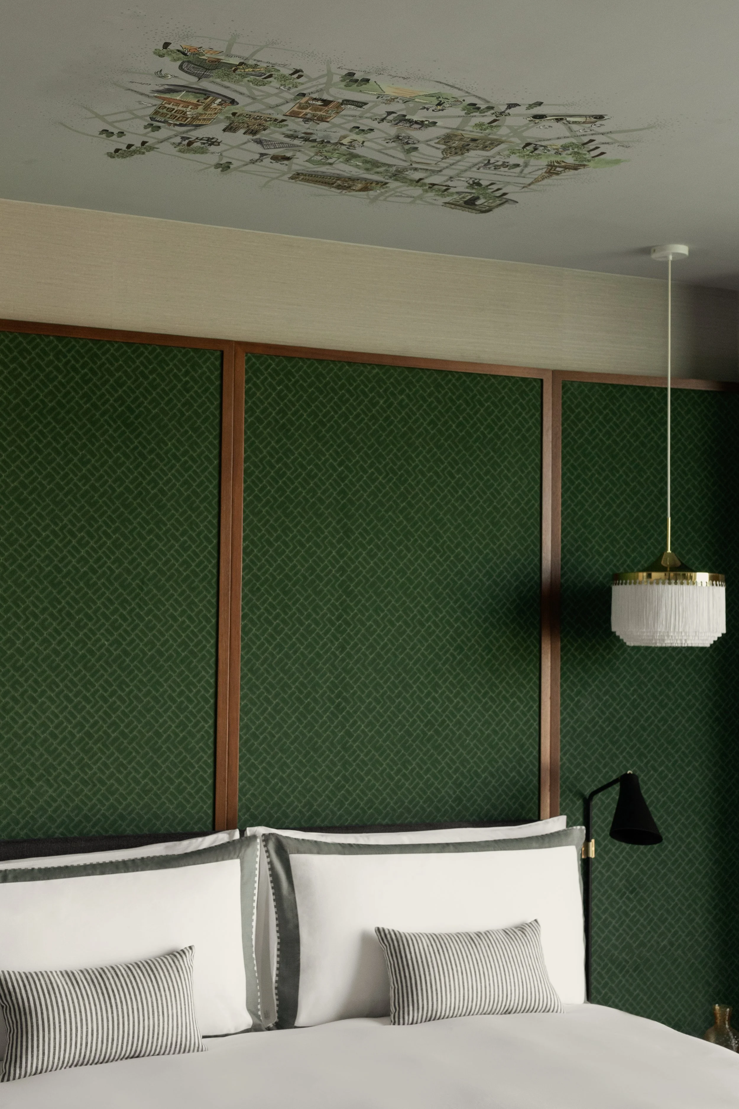 A bedroom with a bed, pillows with striped patterns, a green textured accent wall, a black wall-mounted lamp, and a ceiling-mounted decorative light fixture.