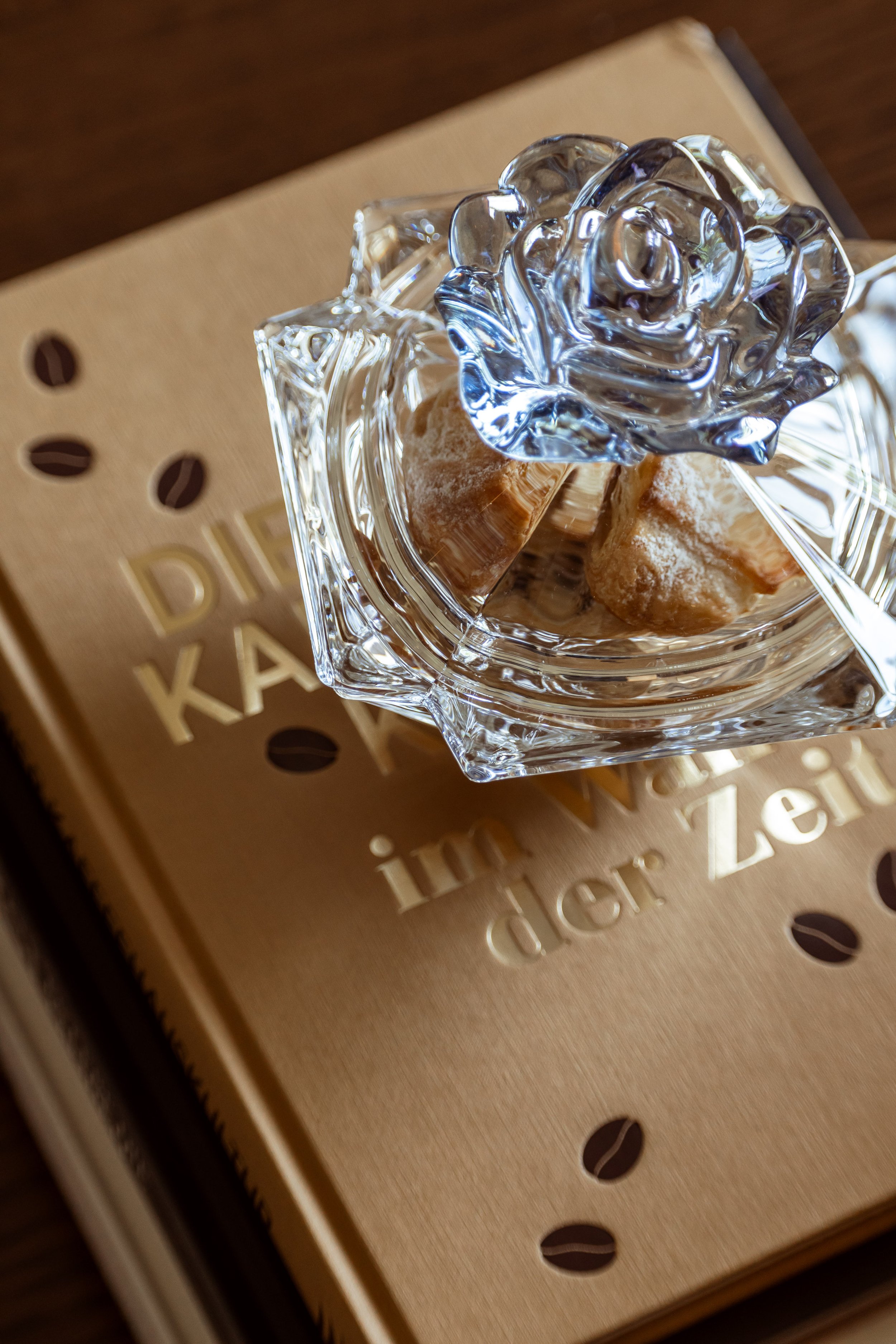 Close-up of a glass decorative flower atop a box of chocolates on a wooden surface.