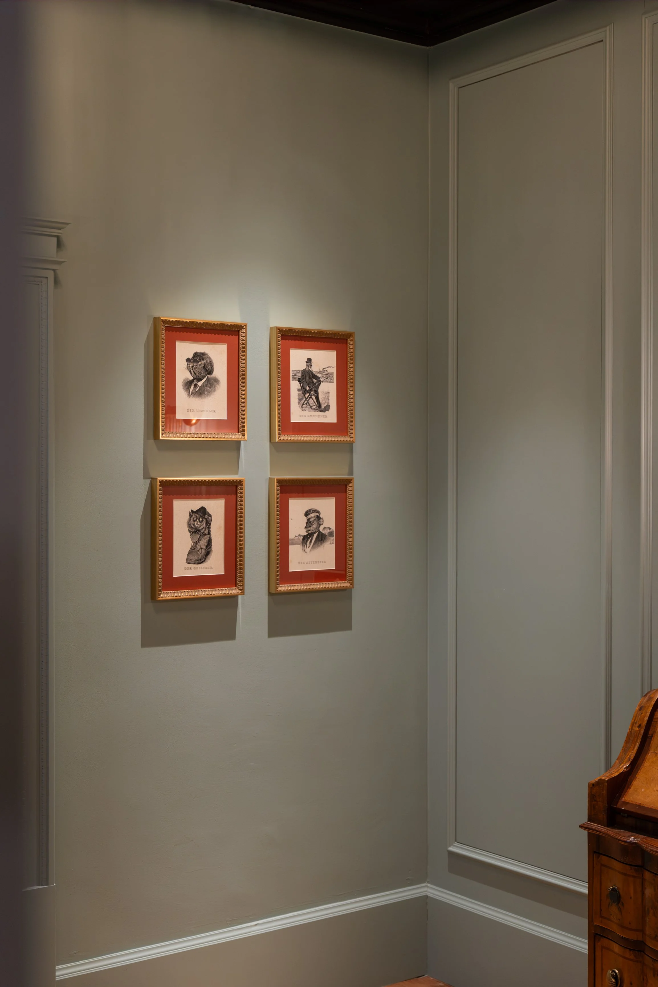 Gallery wall with four framed black and white illustrations of animals dressed in human clothing on a light-colored wall in an indoor setting.