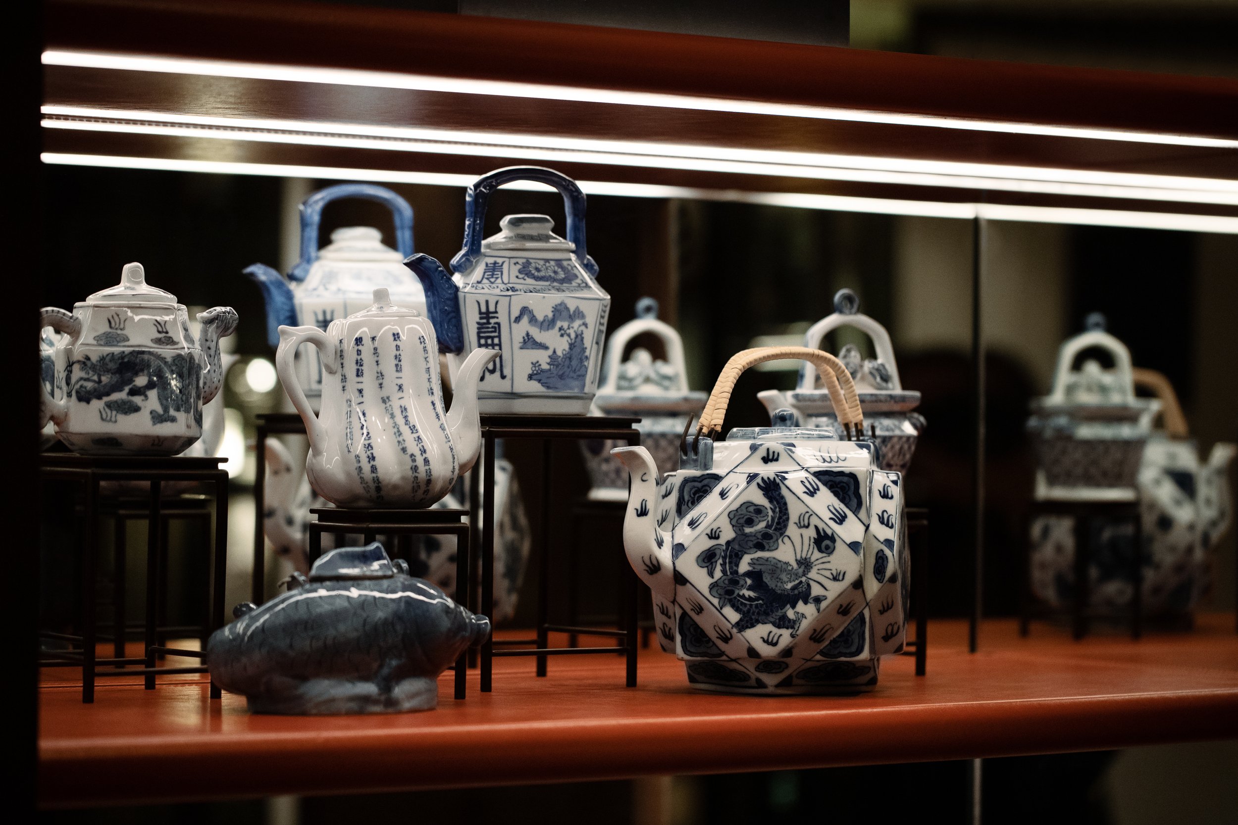 Display of blue and white porcelain teapots with Chinese designs on a wooden shelf with a mirrored background.
