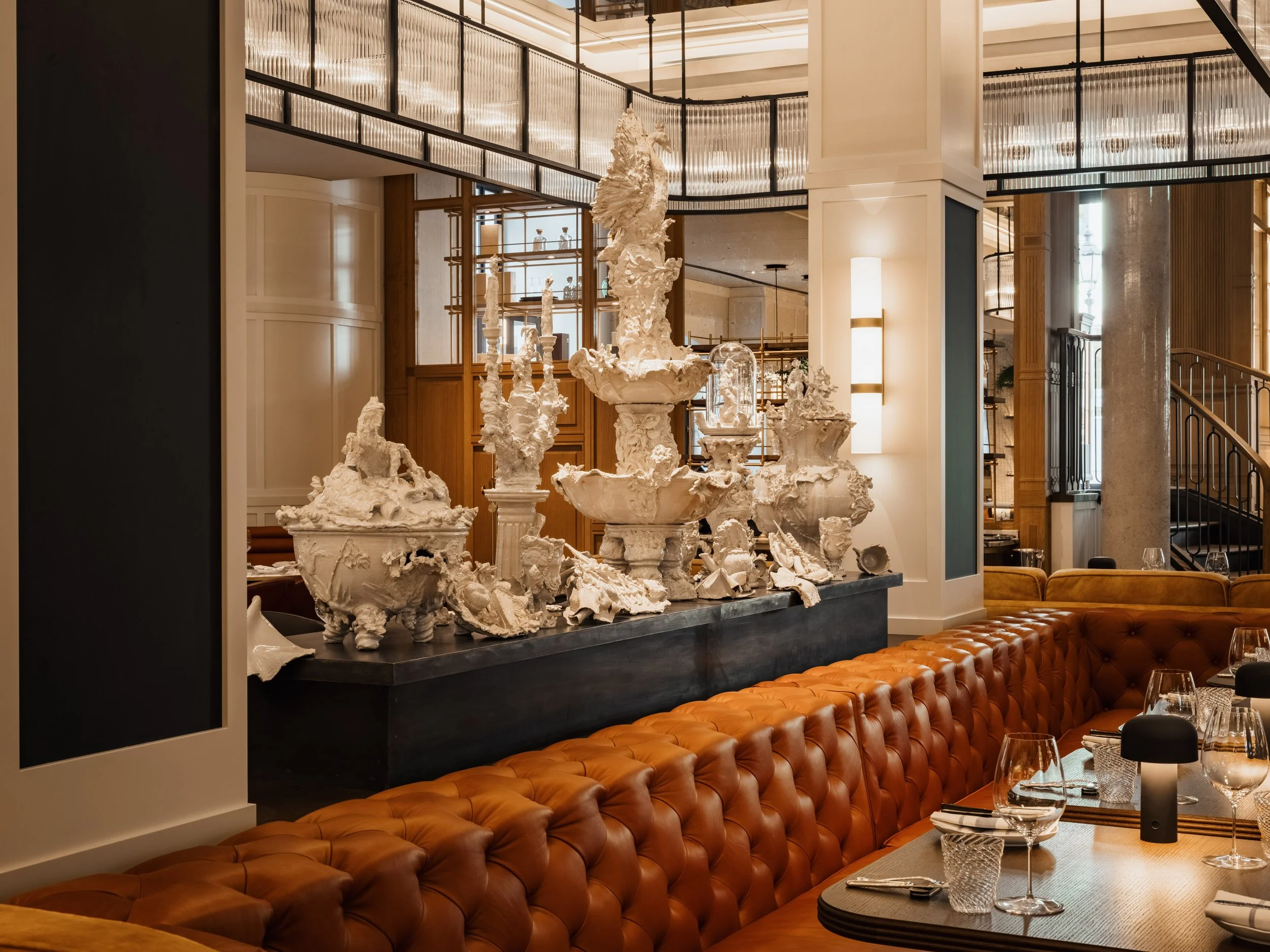 Elegant restaurant interior with ornate white sculptures on black displays, wood accents, and a curved glass ceiling feature.