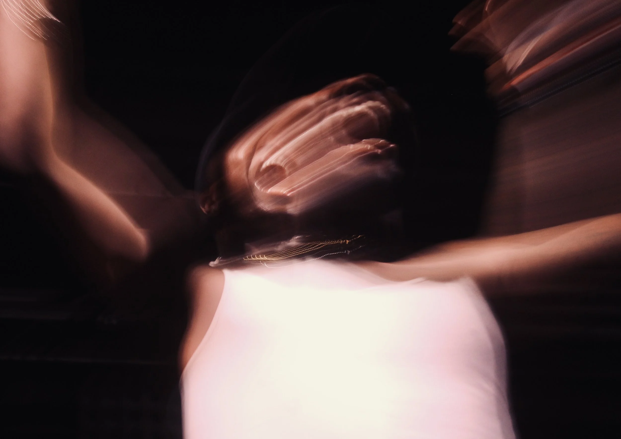 Abstract motion-blurred photograph in dark tones with streaks of light and soft glowing shapes.