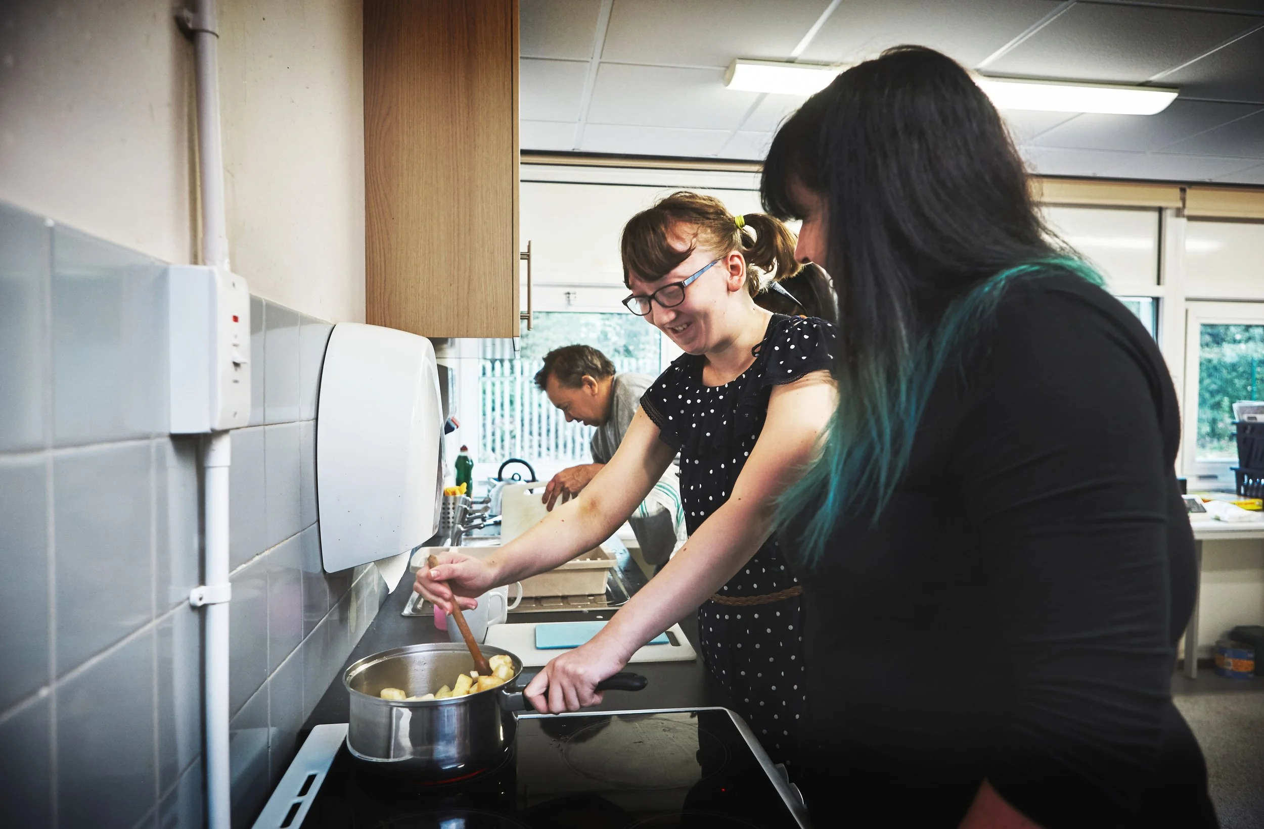 Two women smiling and cooking together in a kitchen as a tbi rehabilitation project.