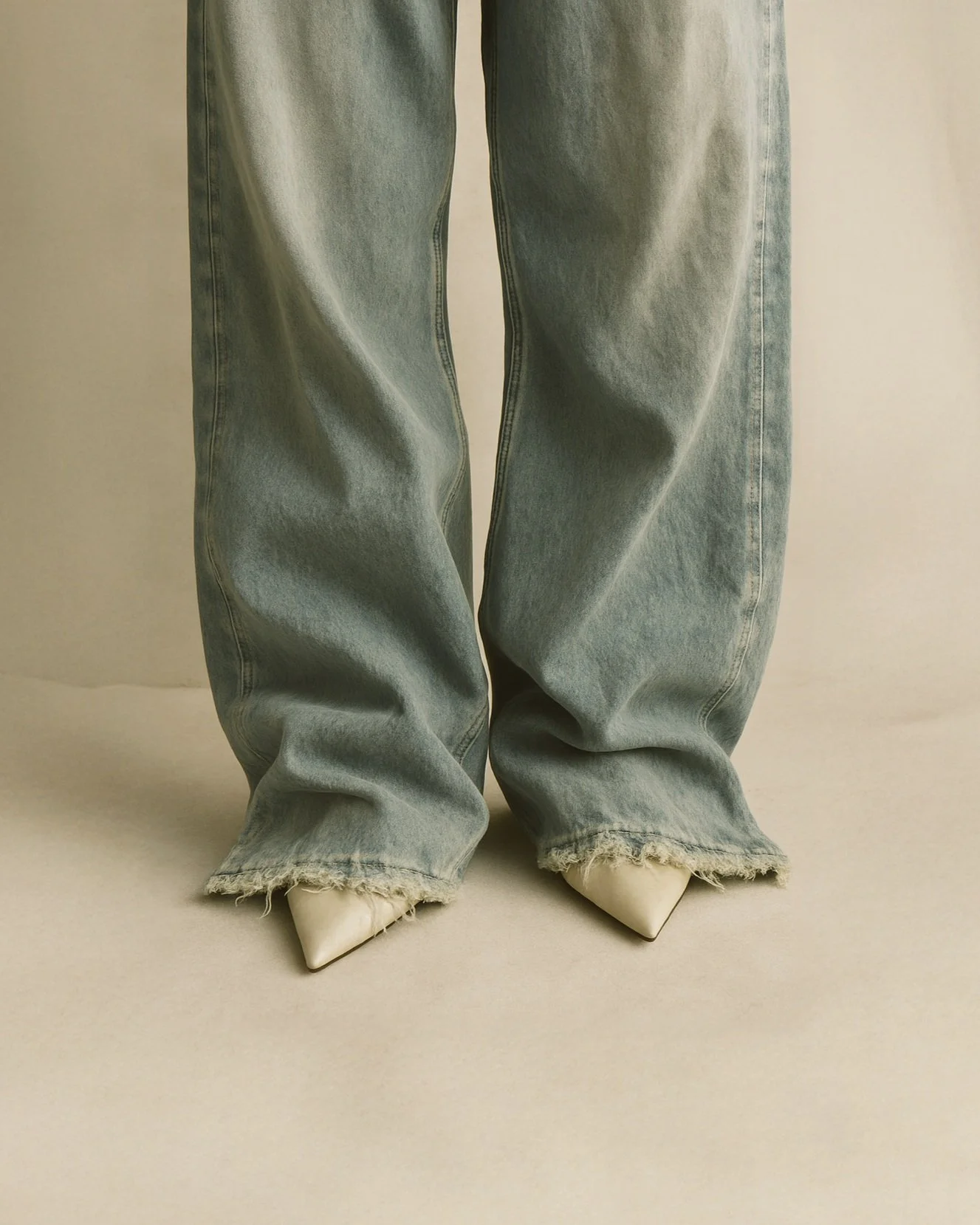 Close-up of person wearing oversized baggy jeans with frayed hems, white pointed shoes visible at the bottom.