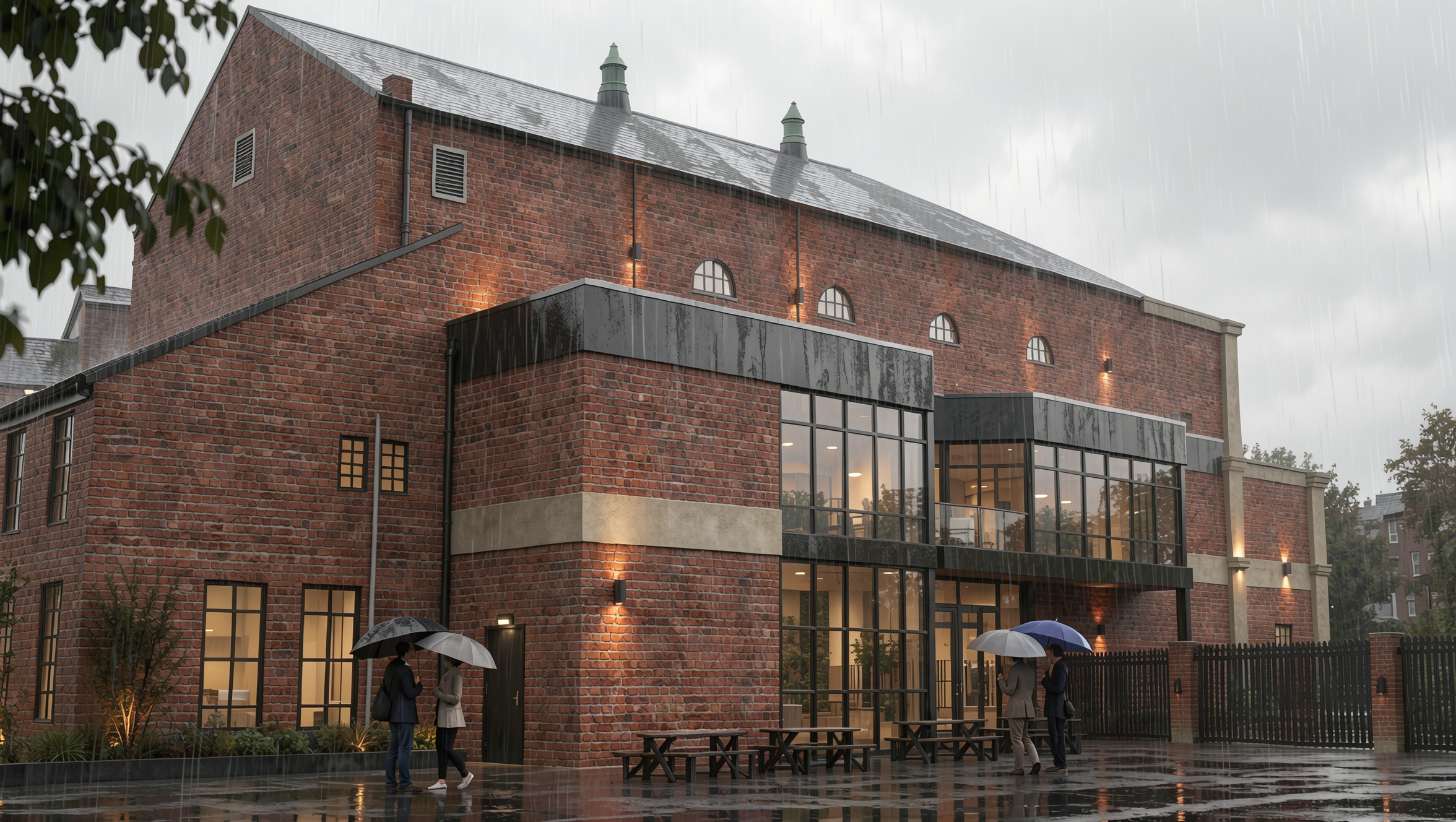 A modern brick building with large glass windows and outdoor lighting, rainy weather with people holding umbrellas outside.