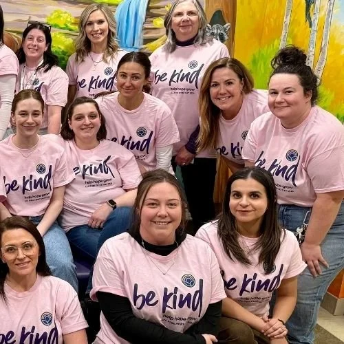 Group photo of LCC staff members smiling at the camera while wearing pink Be Kind t-shirts