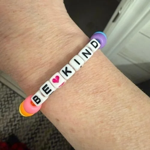 Close up of multi-coloured friendship bracelet with the words BE KIND