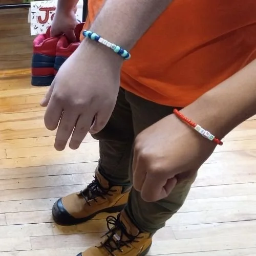 Close up view of two youth's wrists wearing their friendship bracelets with the words "kind" on them