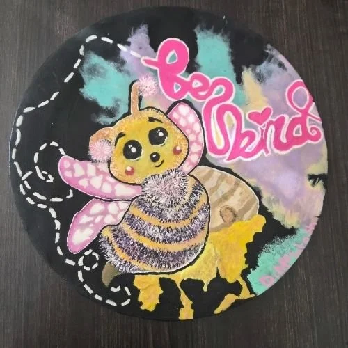 Youth created anti-bullying artwork with a painted bee and a colourful background with the words "be kind" in bright pink