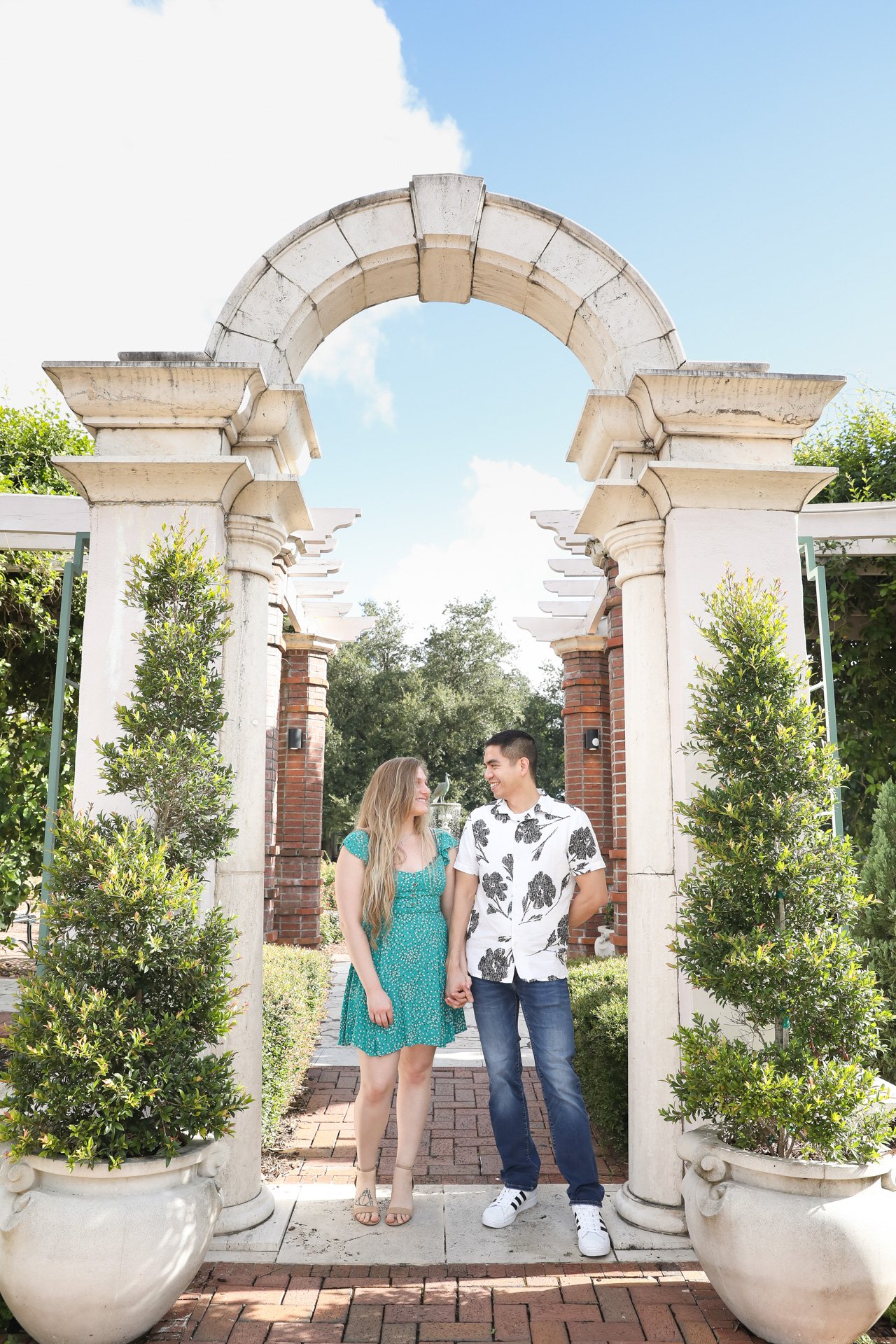 Couple holding hands under stone archway in a garden setting.