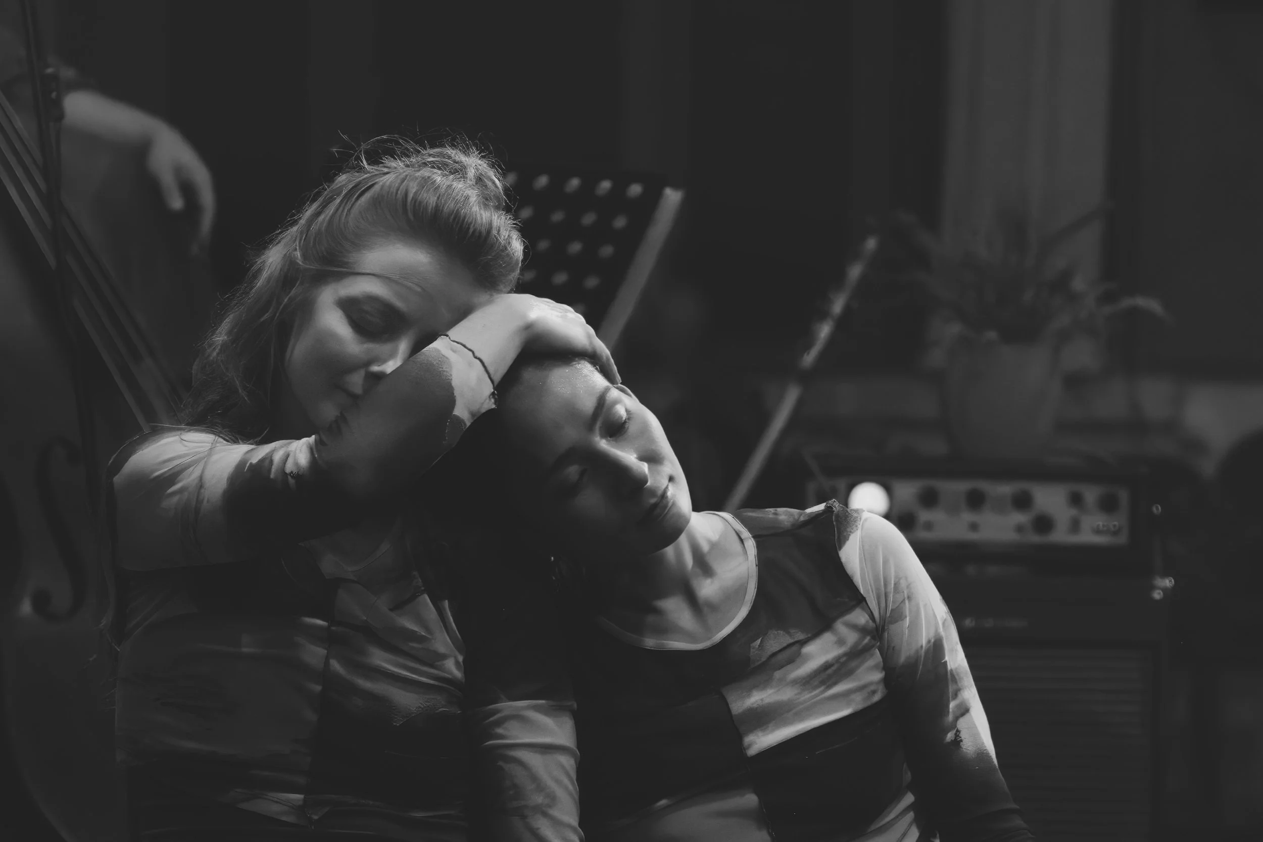 A woman resting her head on a man's chest with her arms around his shoulders in a dimly lit room, possibly a music or recording studio.