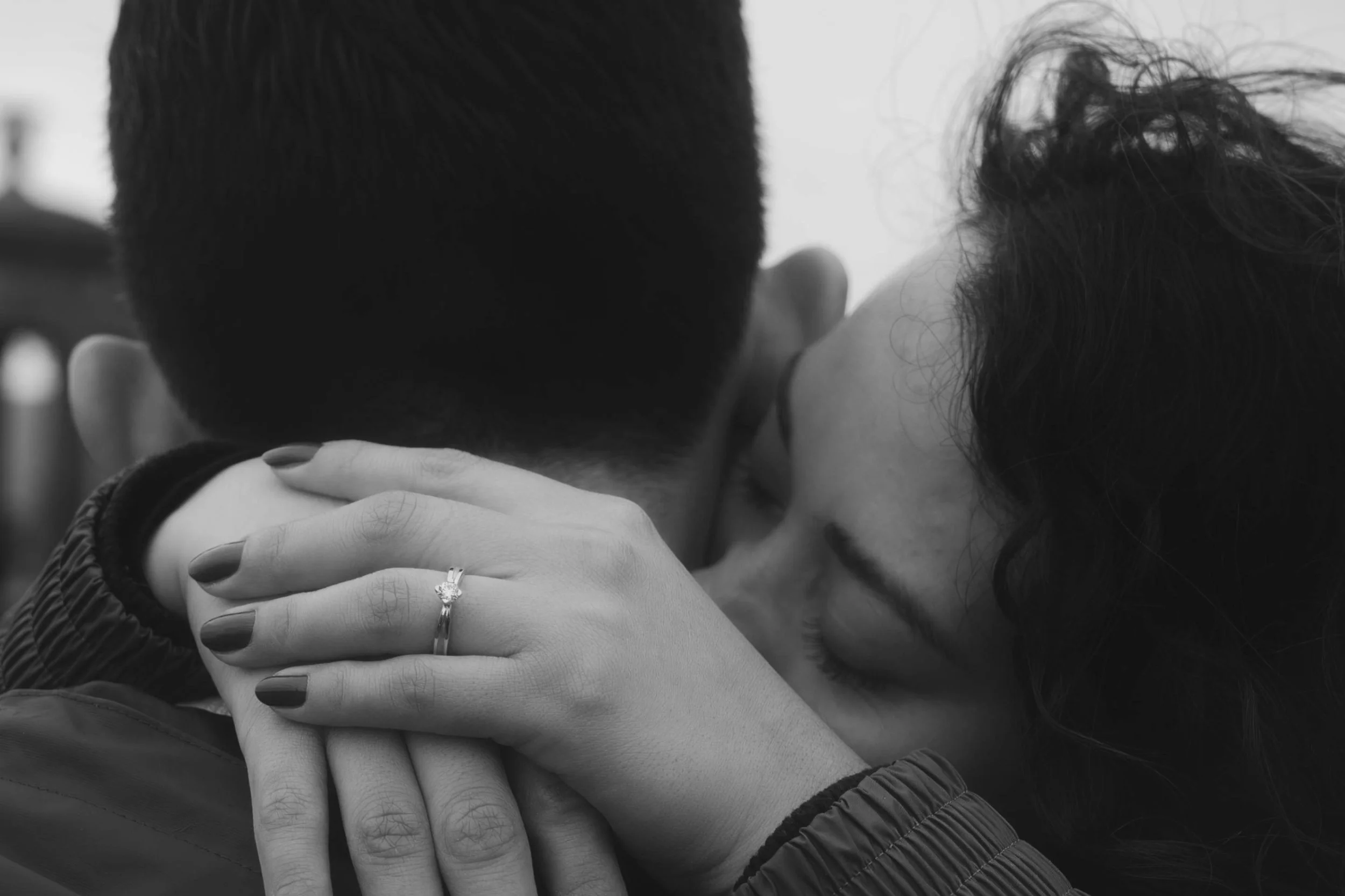 Couple sharing a kiss, with intimate embrace, close-up of hands and faces in black and white.