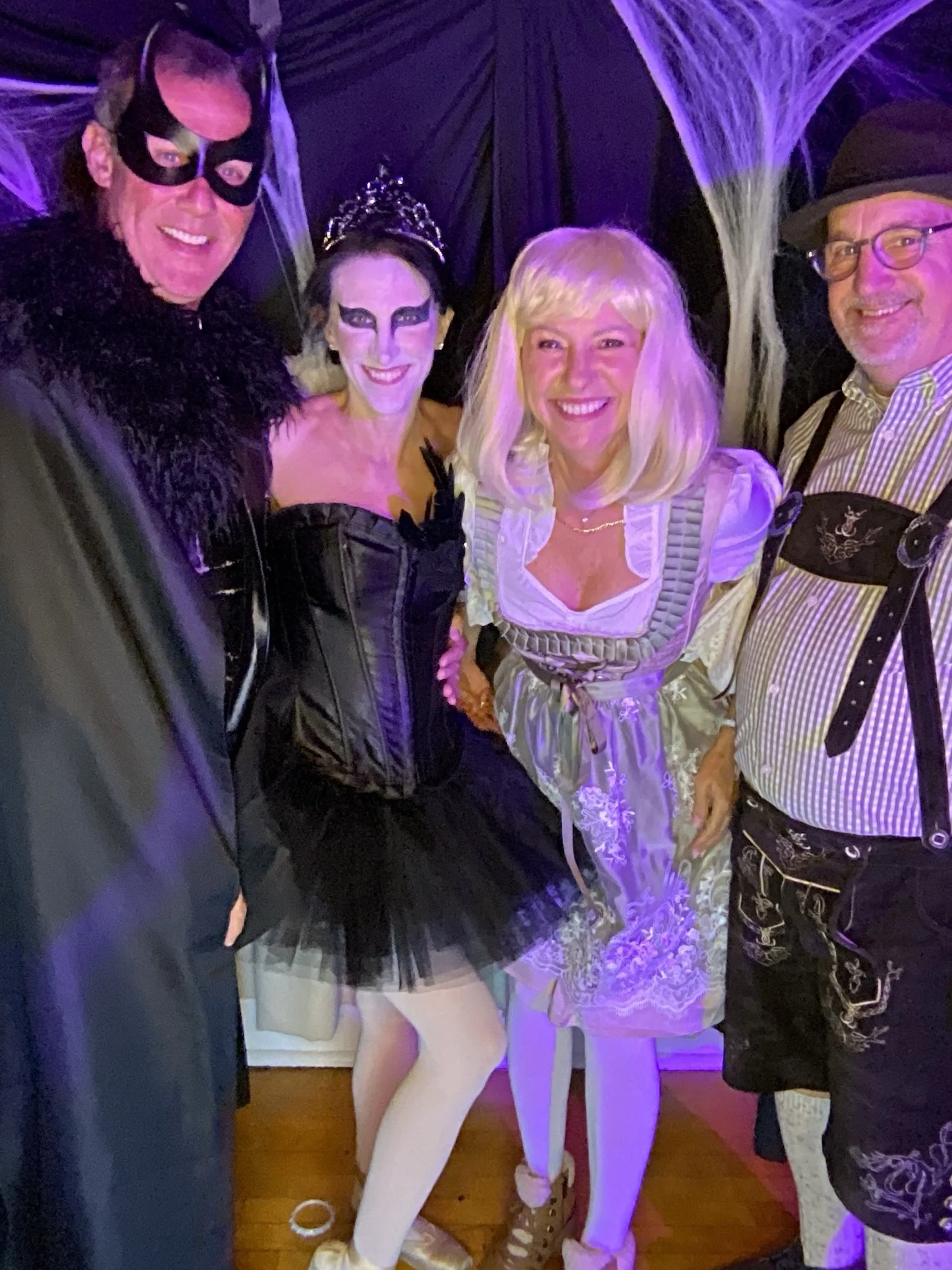 Five people dressed in costumes posing for a group photo at a costume party, with dark and spider-web decorations in the background.