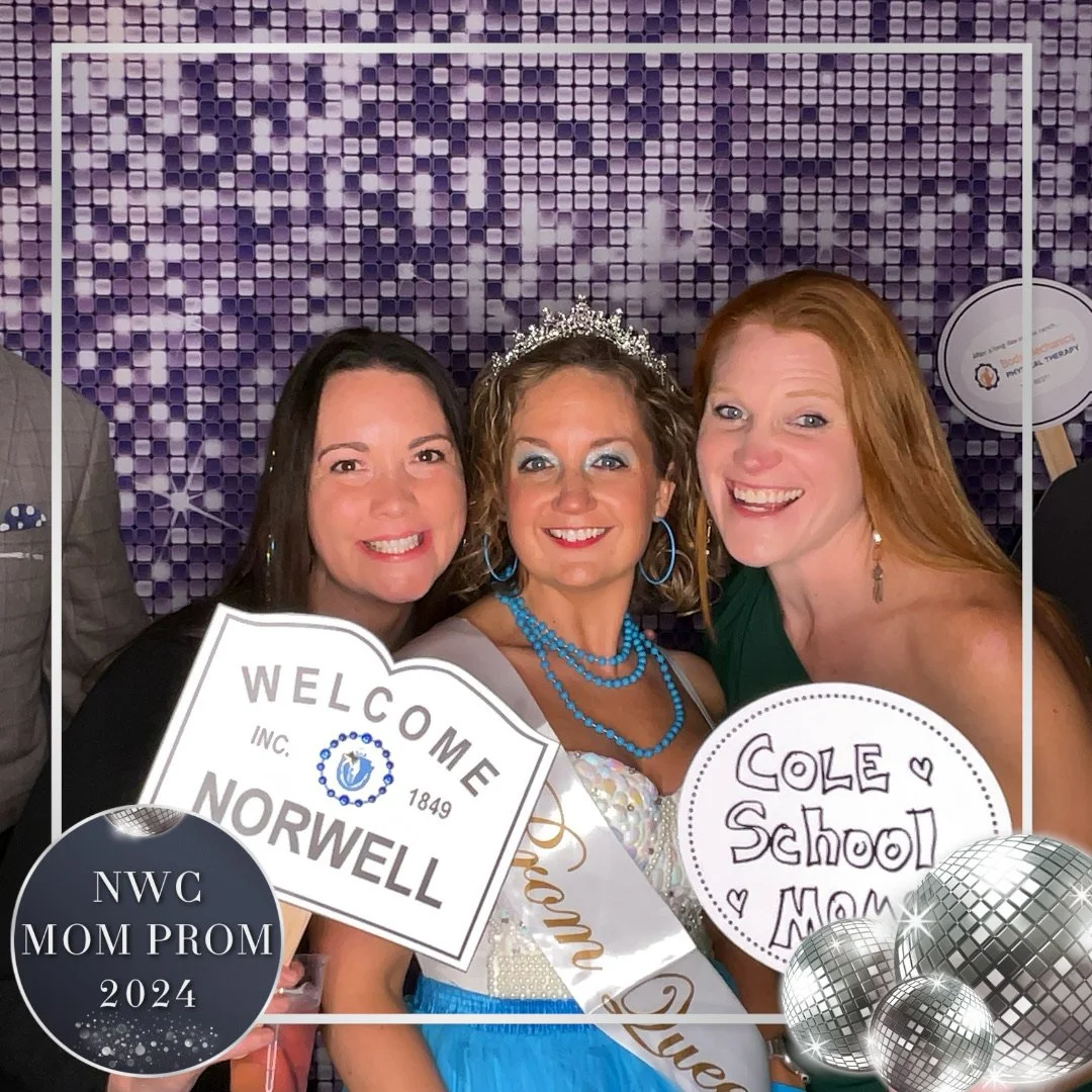 Three women celebrating at a prom event, one dressed as a princess with a tiara and sash, holding signs that say "Welcome Norwell" and "Cole School Mom." The background has a purple mosaic pattern with a bubbly border and silver disco balls, indicati