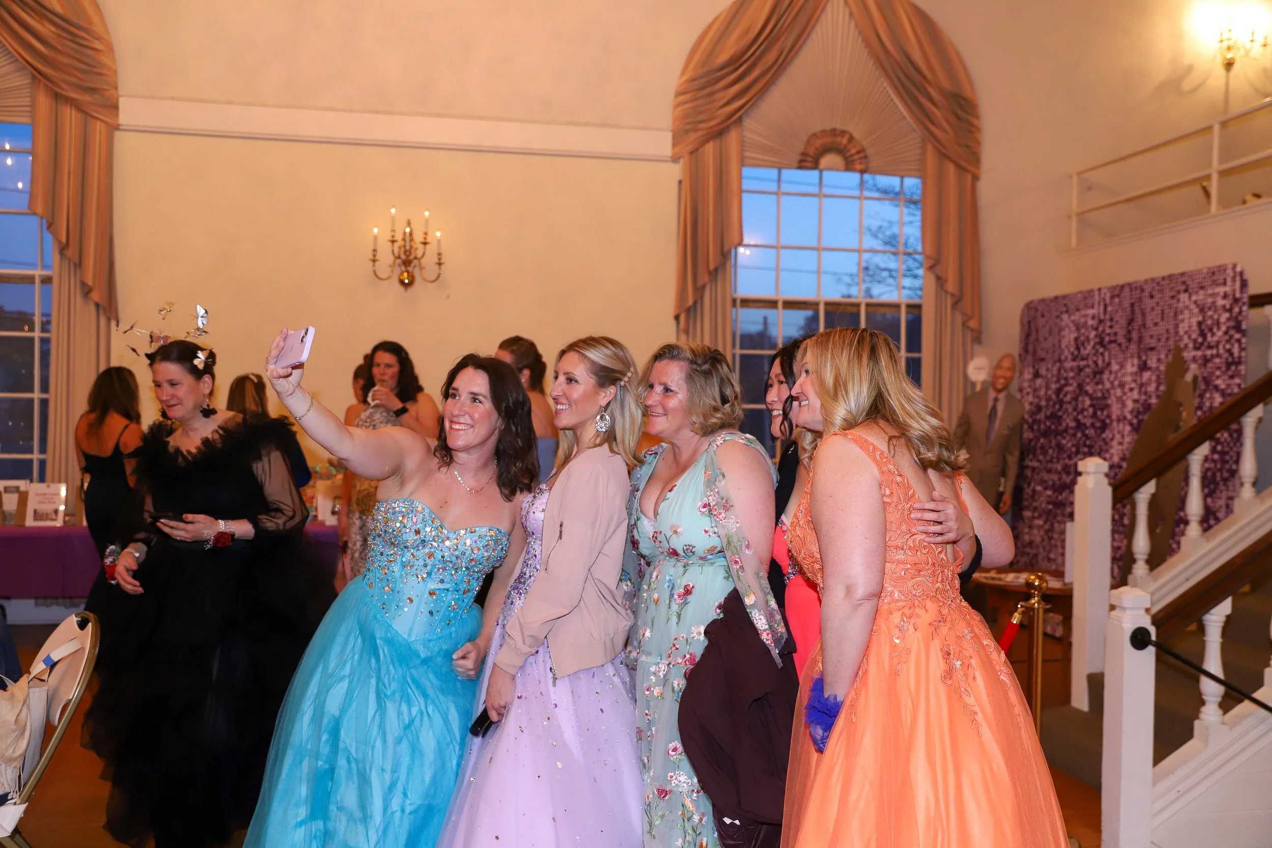 Group of women in colorful dresses taking a selfie at an elegant indoor event.