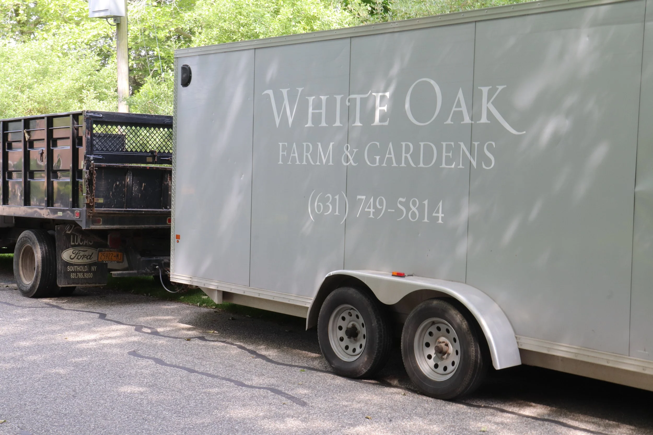 An image of a landscaping trailer that reads White Oak Farm & Gardens with a telephone number.