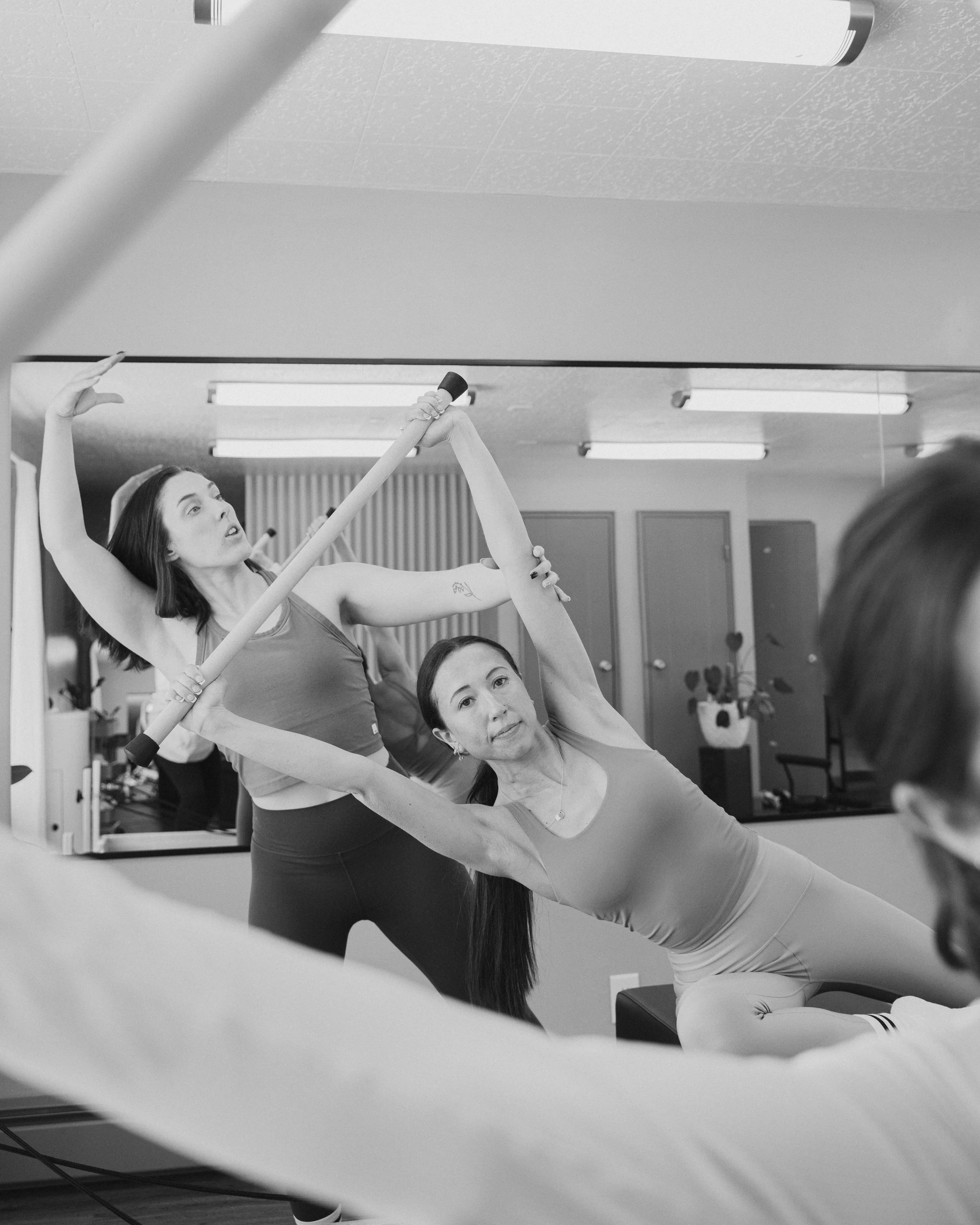 an instructor assisting a student in a side bend on top of a reformer at goodbody pilates and flow