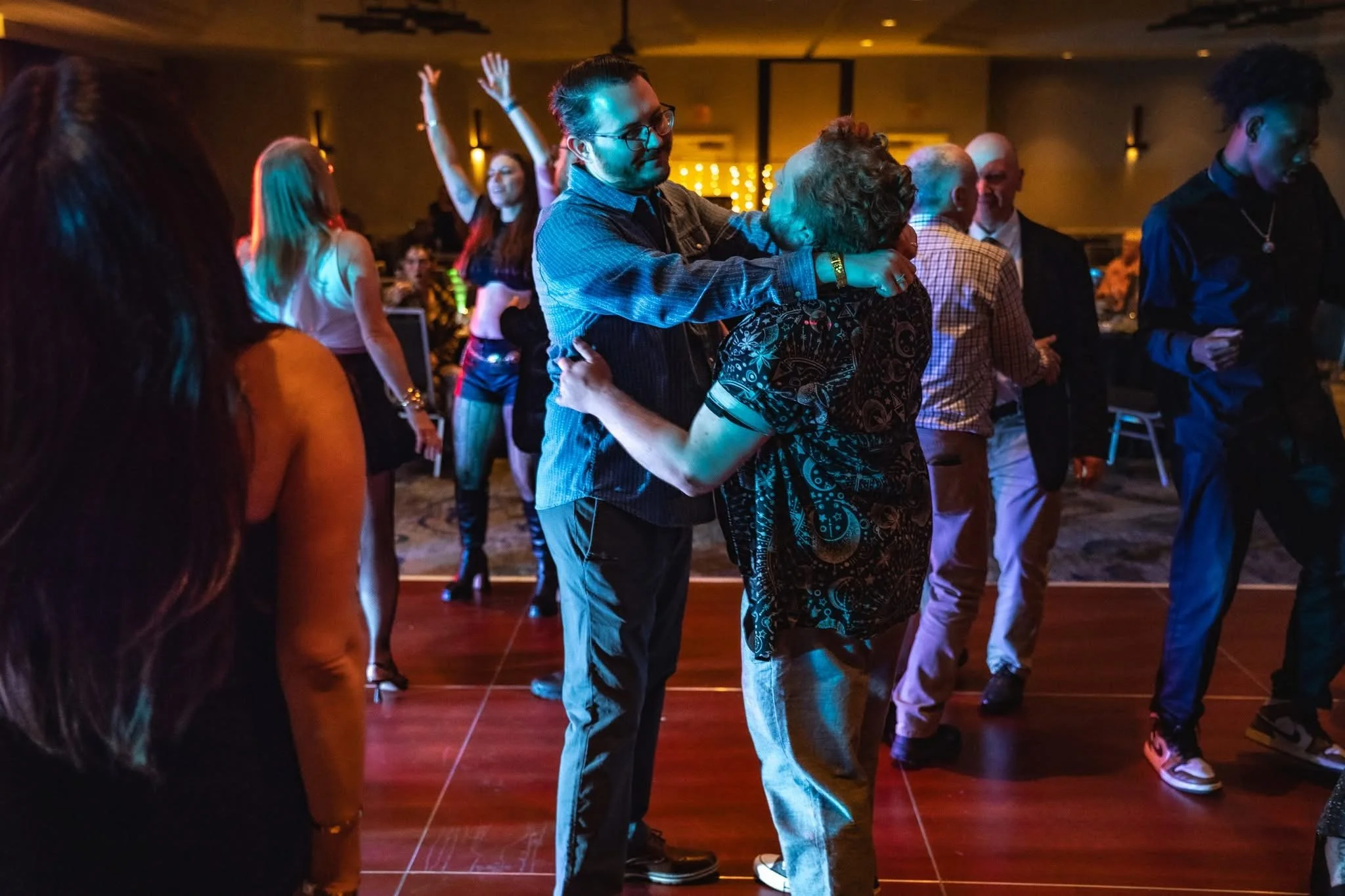 People dancing and hugging at a party or celebration in a dimly lit venue.
