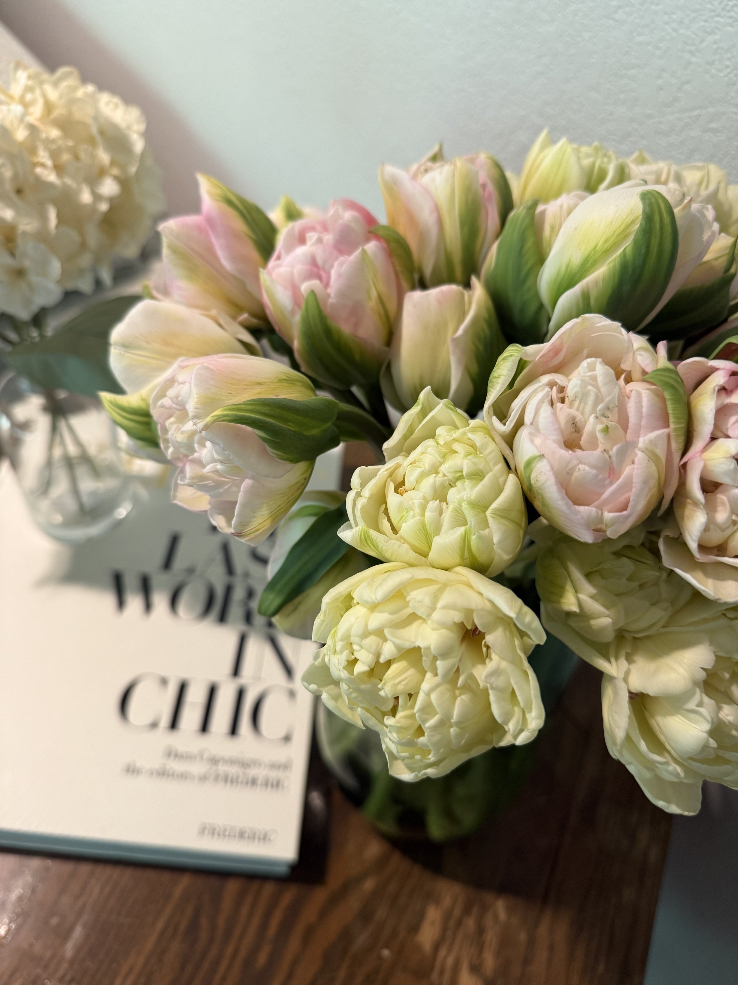 Bouquet of pink and white tulips in a vase on a wooden table with a book
