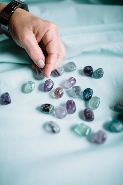 A hand picking up colorful polished stones with gold accents on a light blue fabric surface.