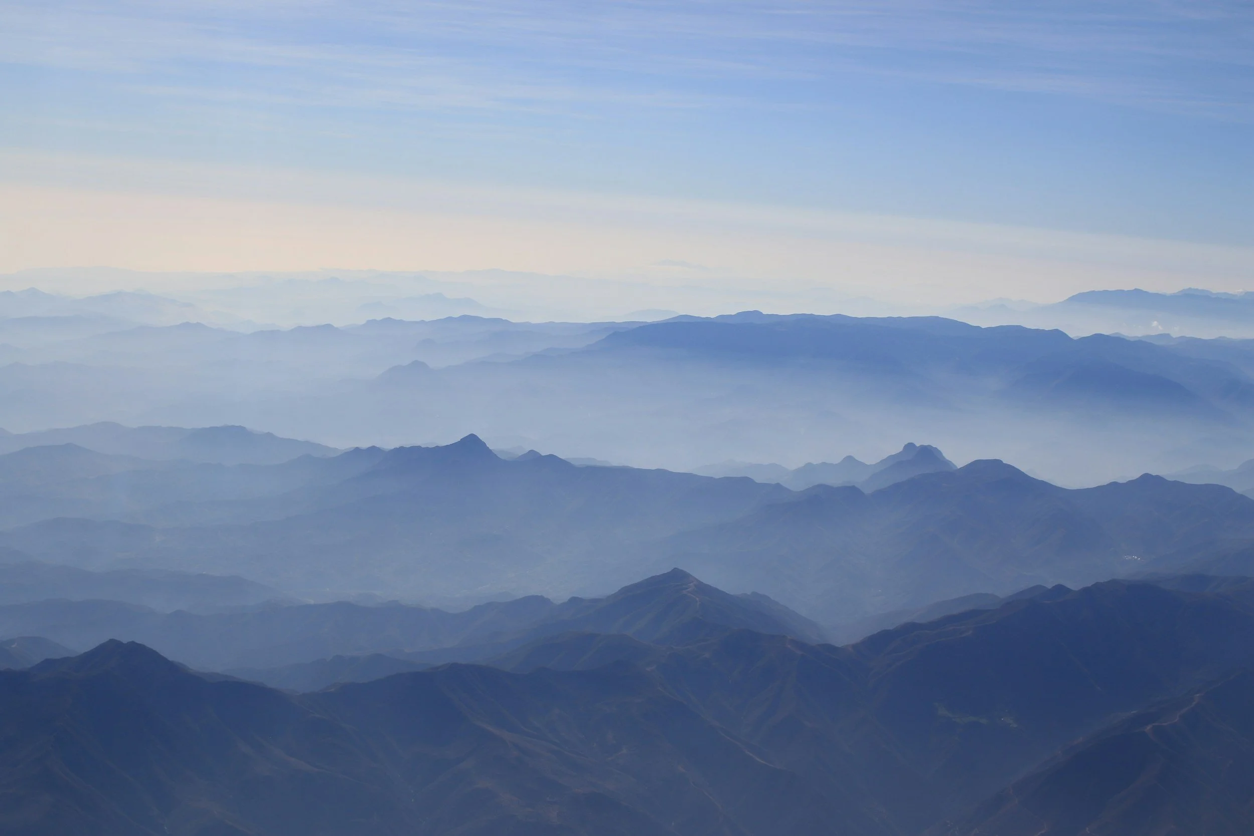 Aerial view of layered mountain ranges under a blue sky with some clouds.