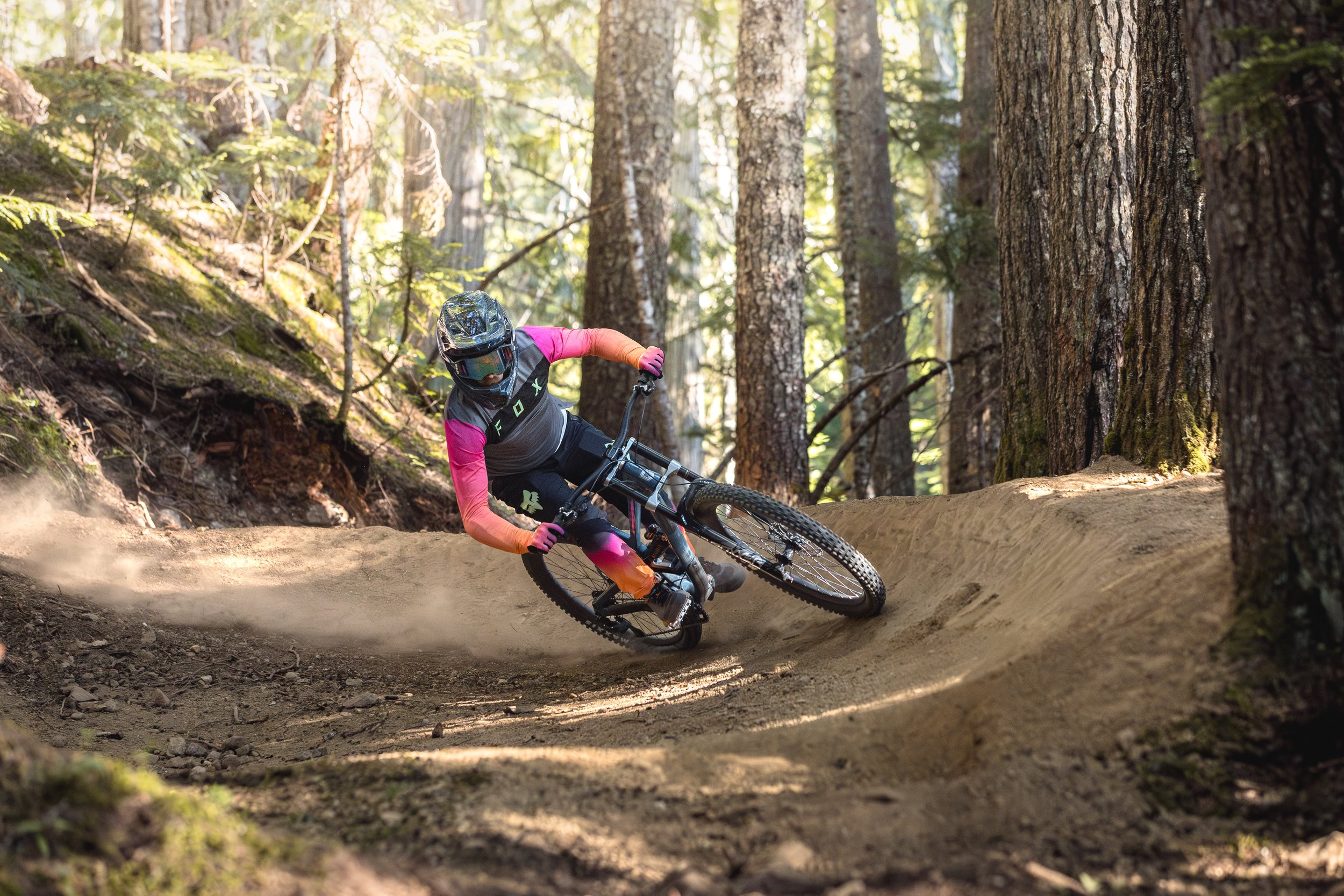 Mountain biker in a forest jumping off a trail on a dirt bike.