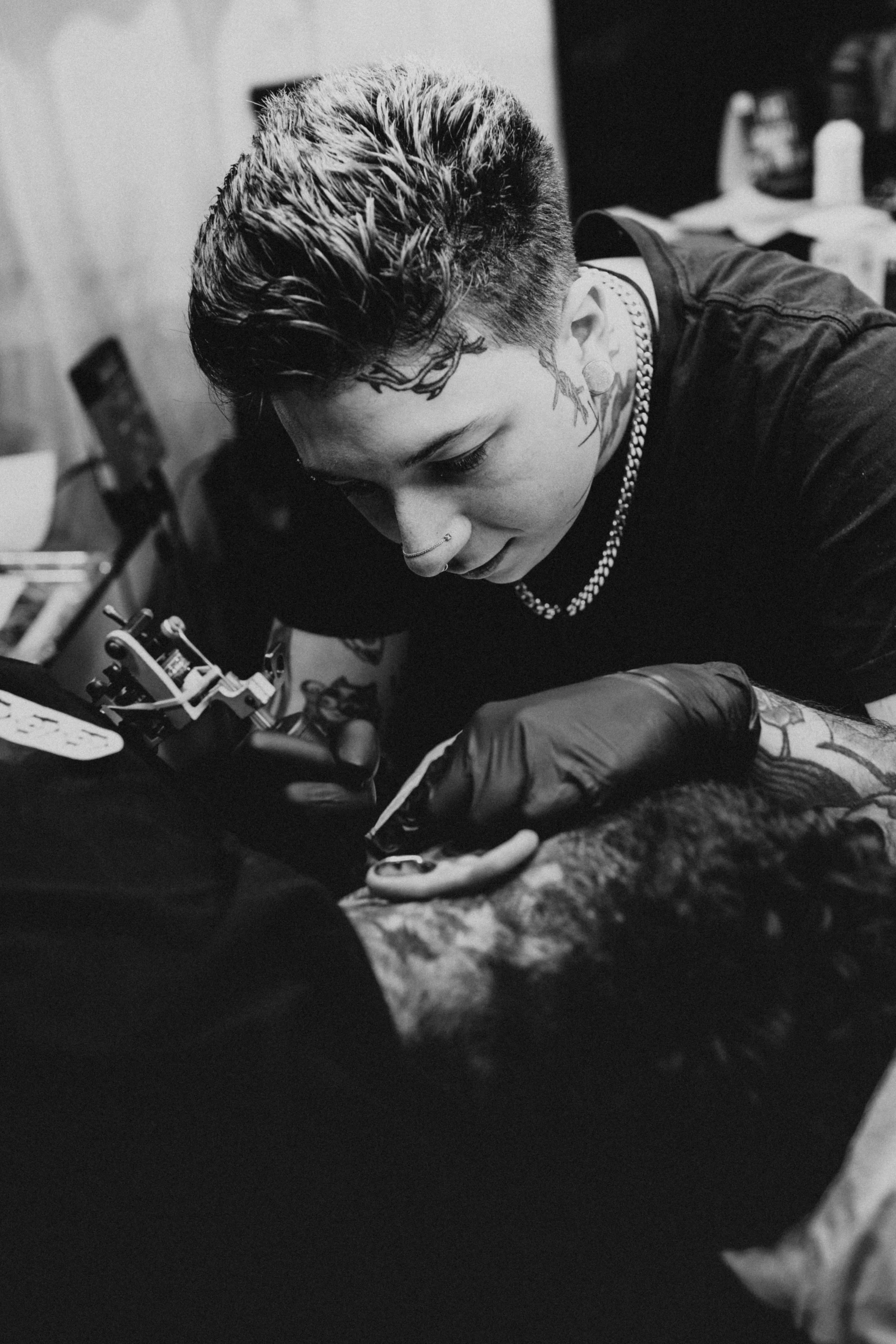 A tattoo artist is working on a client's arm in a tattoo studio, depicted in black and white.