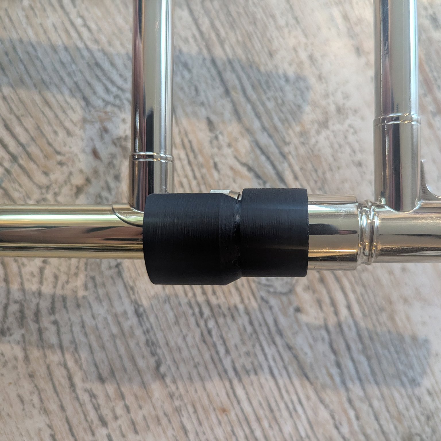 Close-up of a brass musical instrument joint with a black protective wrap against a wooden background.