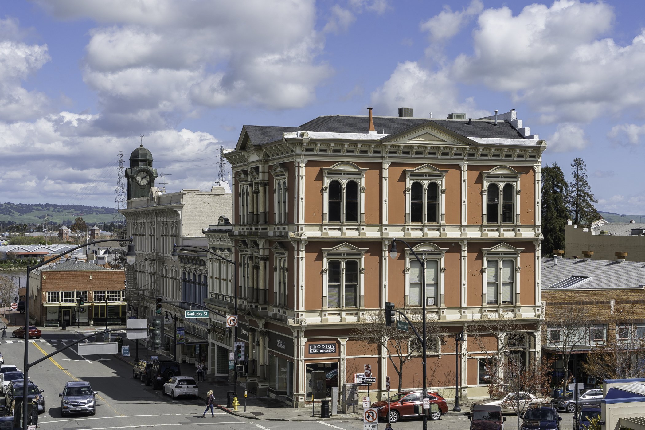 Historic downtown with a clock tower and Victorian-style buildings under a cloudy sky.