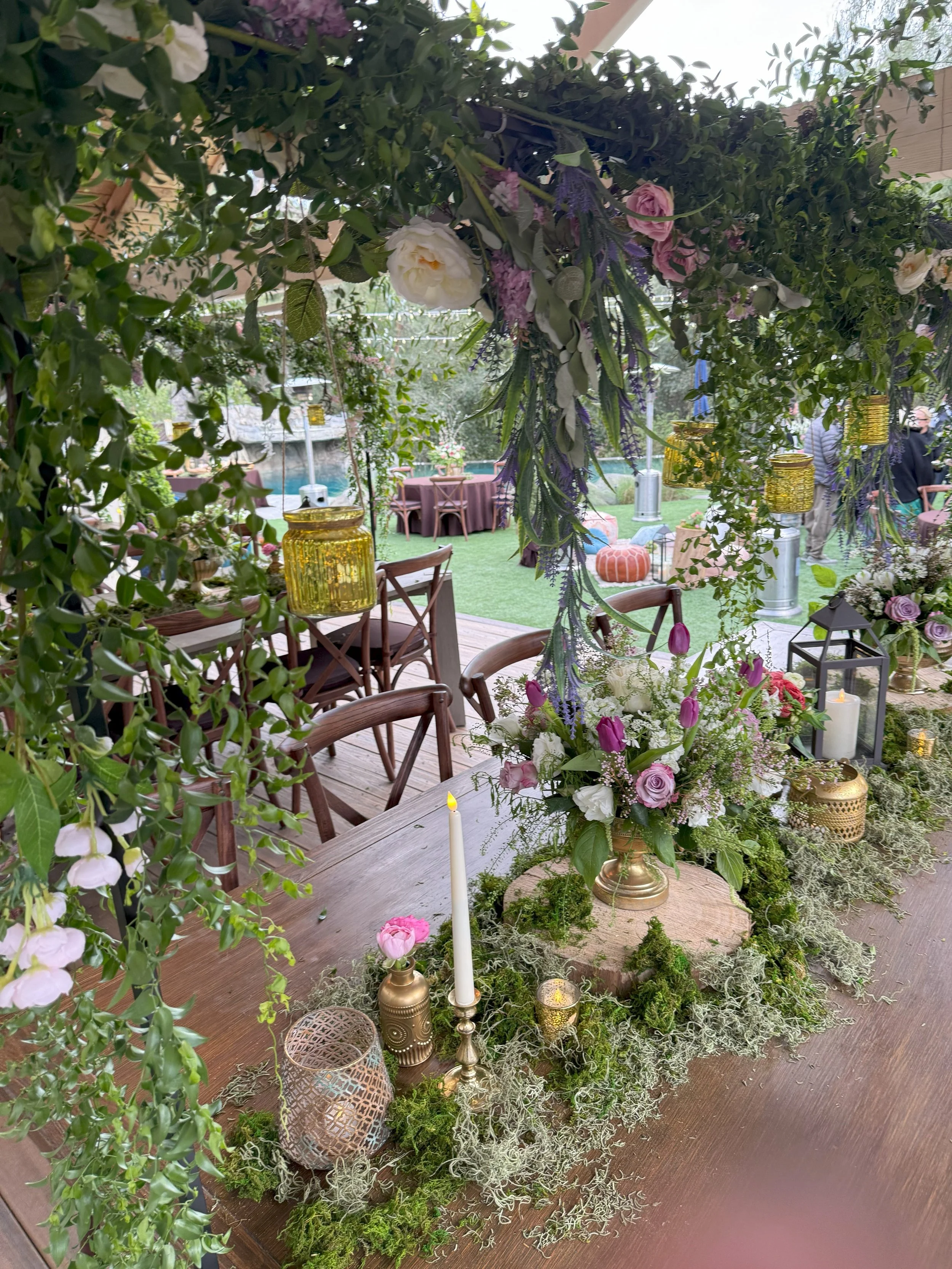 Outdoor wedding ceremony setup with chairs, flower arrangements, a floral arch, and umbrellas in a garden.