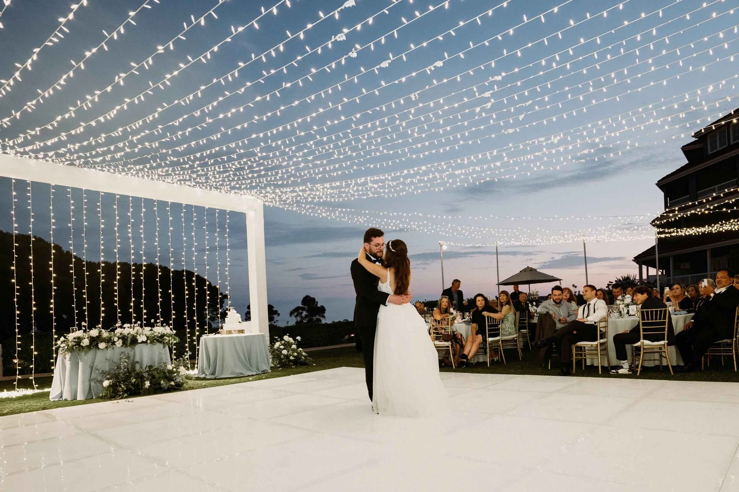 Outdoor wedding ceremony setup with chairs, flower arrangements, a floral arch, and umbrellas in a garden.