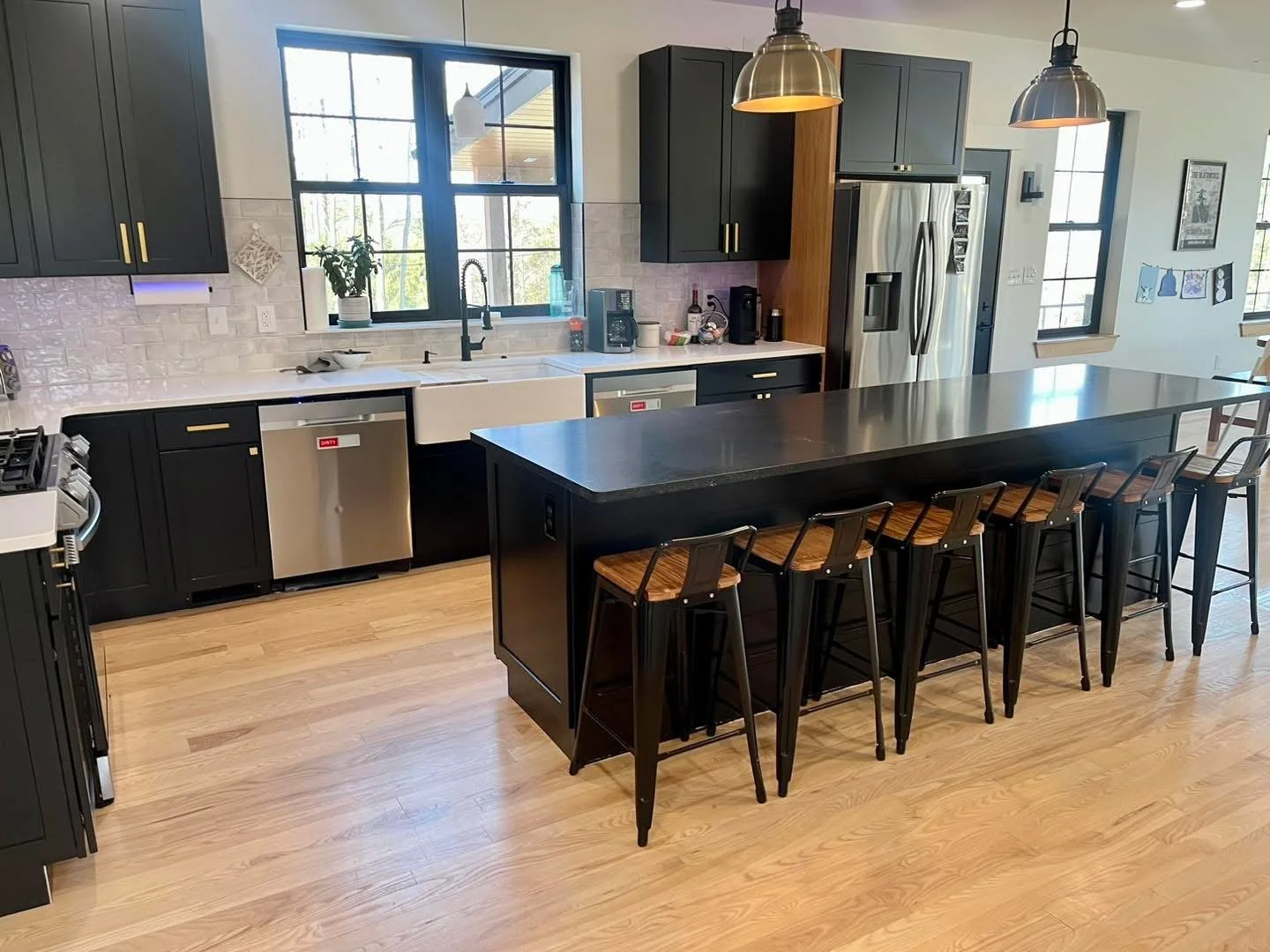 Modern kitchen with black cabinets, a large black island with barstools, stainless steel appliances, hardwood floors, and two pendant lights.