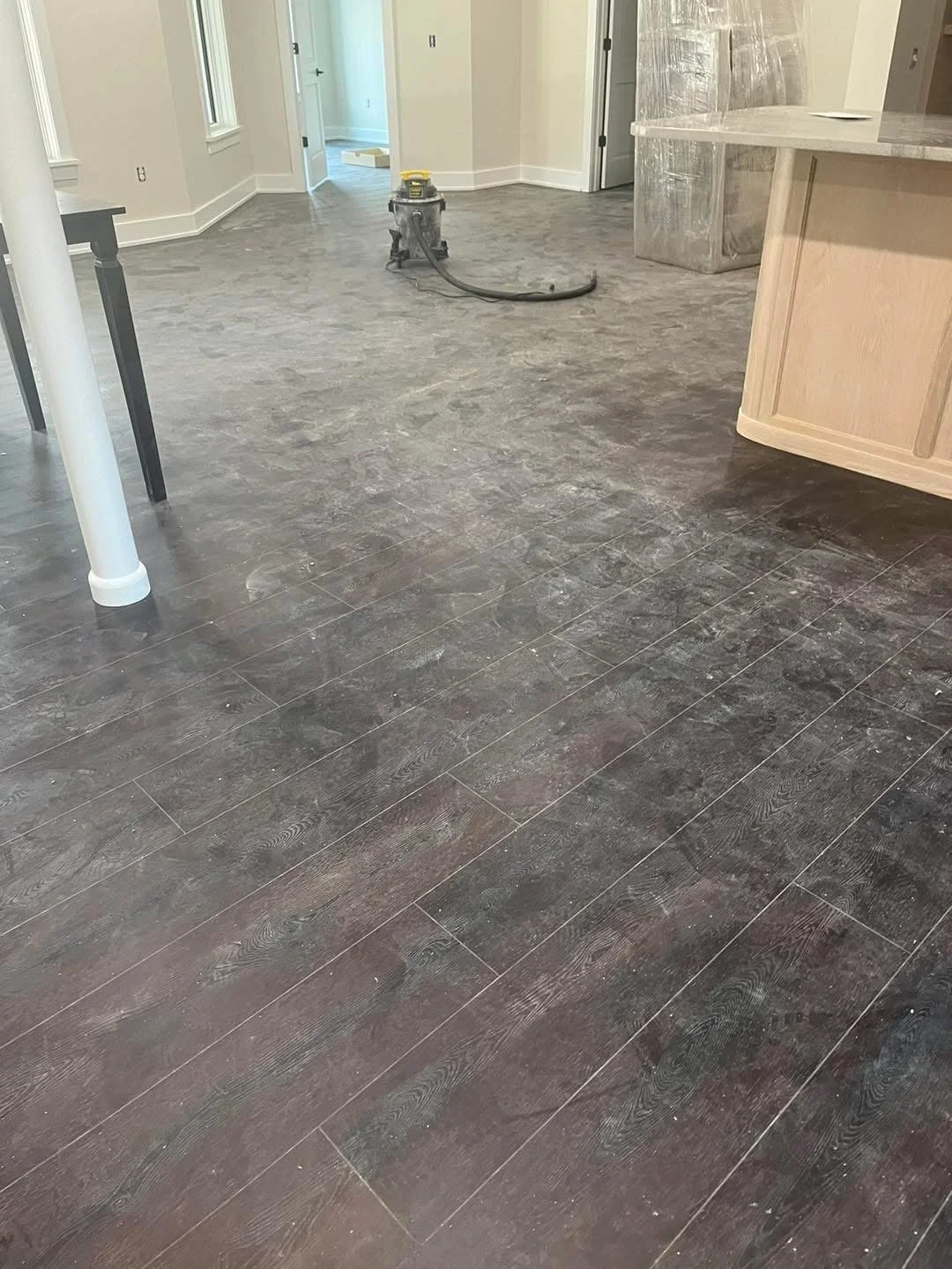 Interior of a room with a newly installed dark wood-look tile floor, a water pipe leading to a machine, and construction materials in the background.