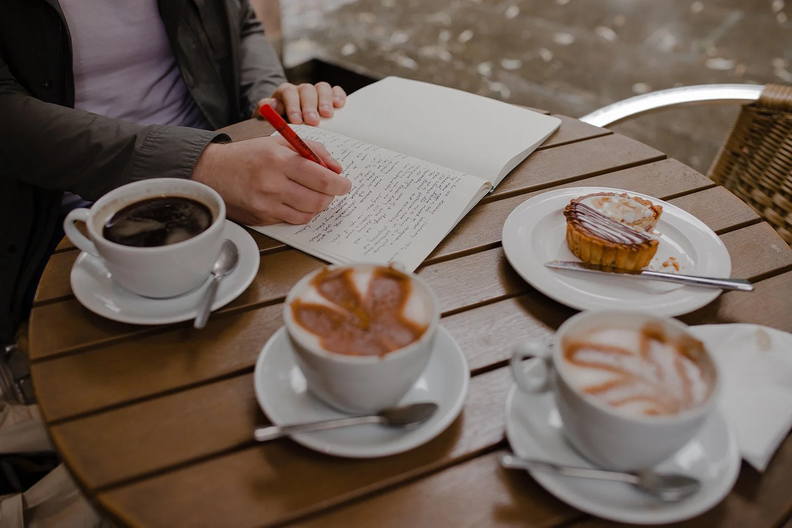 Music teacher writing thoughtfully in a notebook at a café table with coffee and cake
