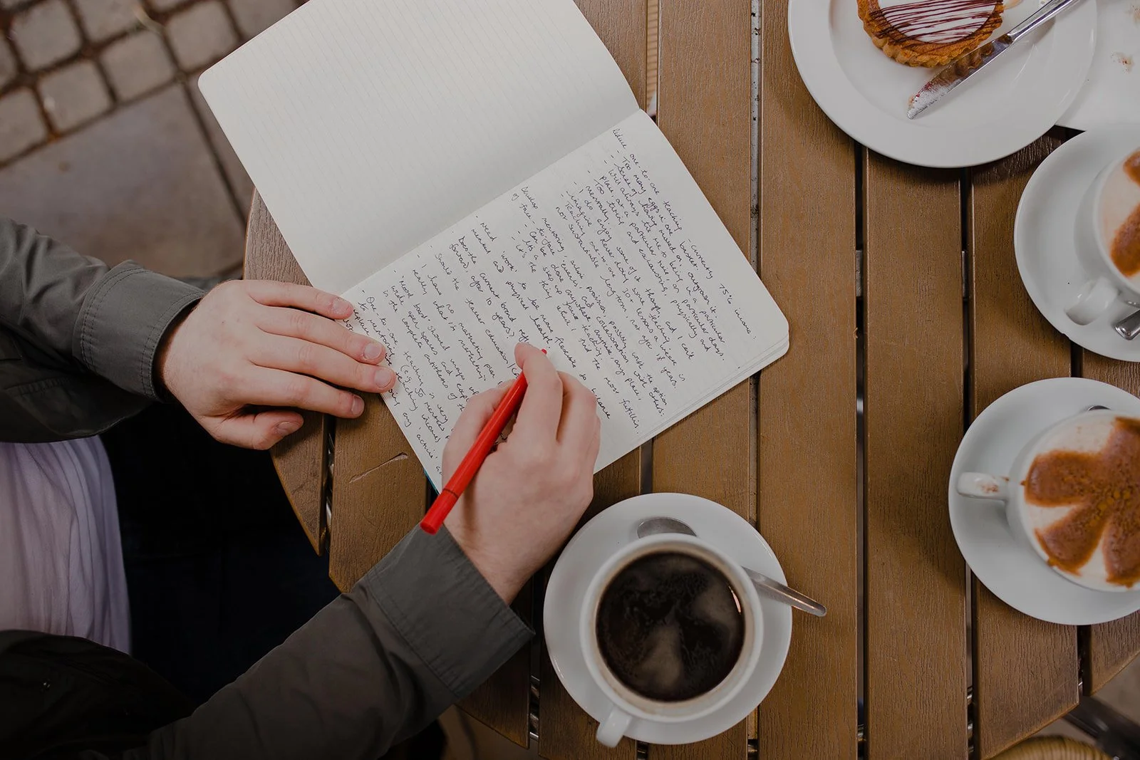 Overhead view of a music teacher writing in a notebook beside coffee and cake in a café
