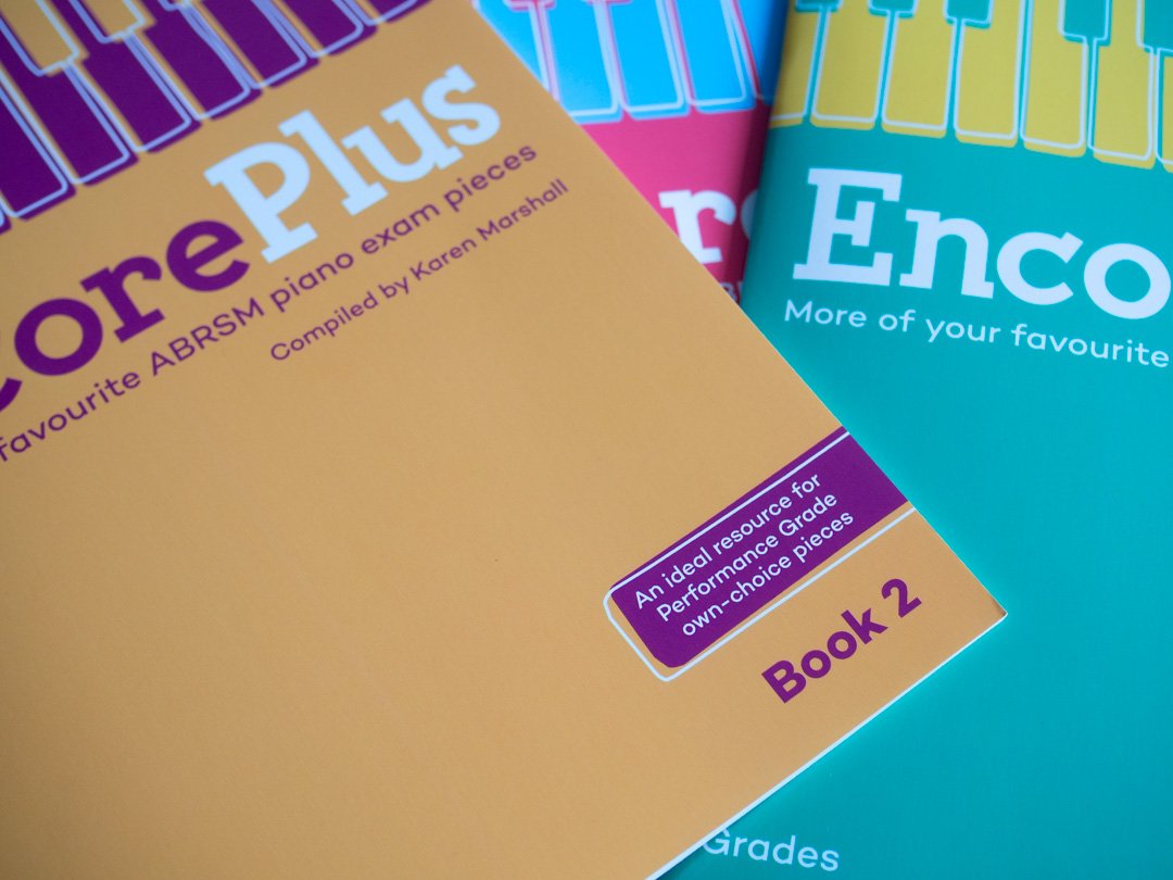 Close-up of the ABRSM Encore Plus Book 2 cover highlighting its connection with ABRSM Performance Grades, with other music books visible behind it.