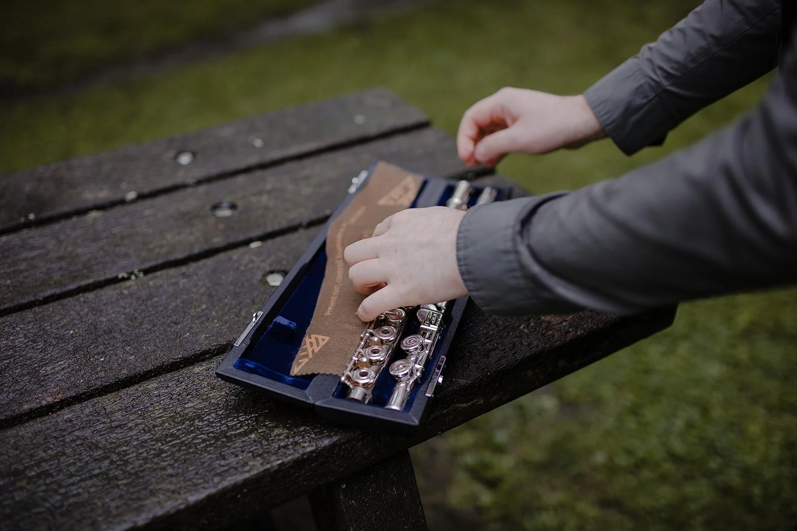 Hands removing a flute from its case outdoors surrounded by nature during a reflective moment as a music teacher