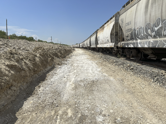 Freight train cars covered in graffiti beside a gravel construction path under a clear blue sky