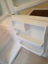 Empty white refrigerator with open door in a room with carpeted and tiled flooring.