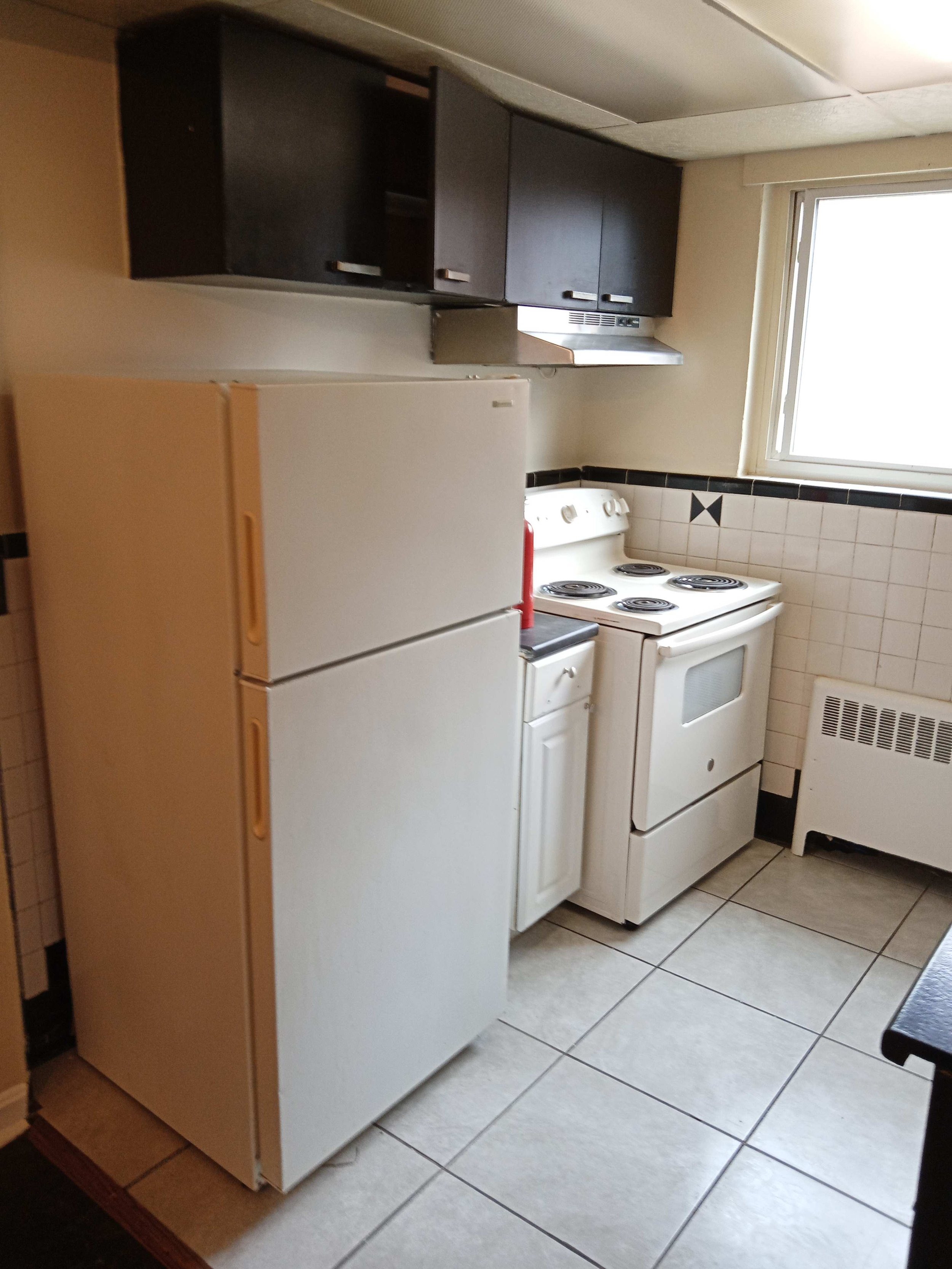 Small kitchen with white refrigerator and stove, black wall-mounted cabinets, a window, and tiled floor.