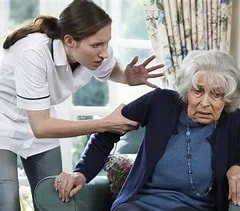 Nurse assisting an elderly woman who looks upset or confused in a care setting.