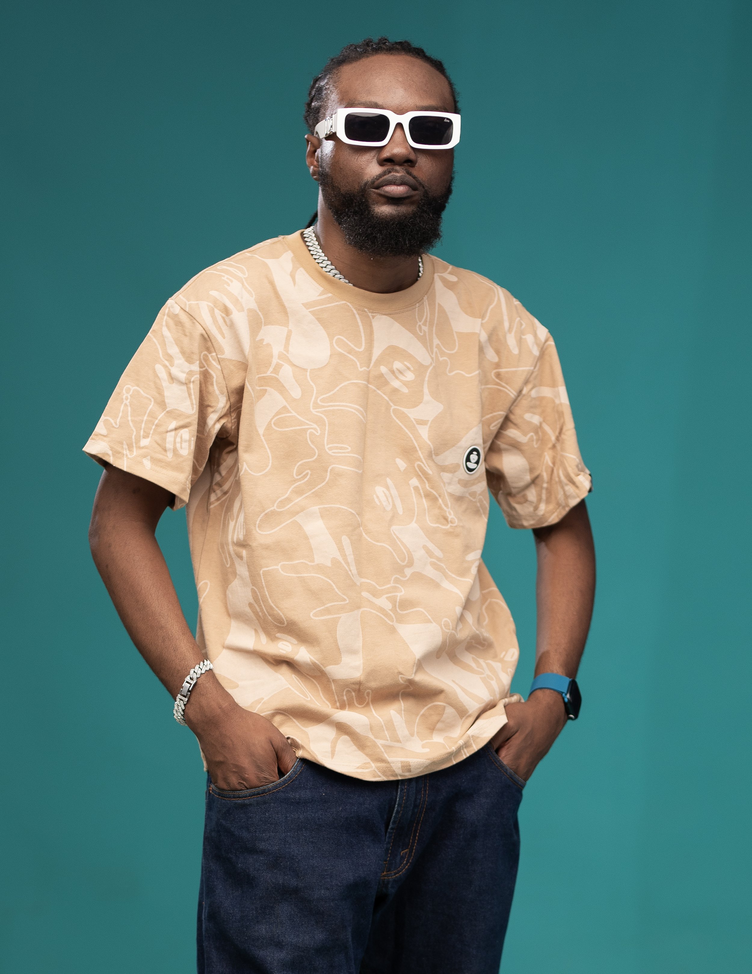 Man wearing beige patterned shirt and white sunglasses against teal background