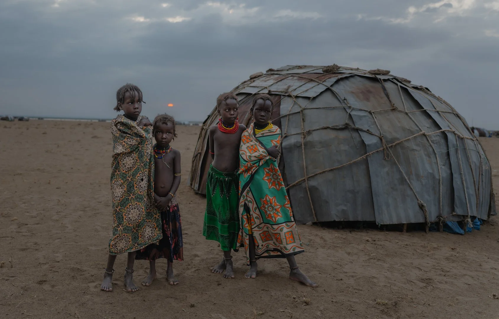 Descalças, com os pés na areia, quatro crianças permanecem diante da cabana, sob a luz do nascer do sol.

Povo nômade do delta do Omo, os Dassanech vivem entre o rio e o deserto, onde vestimentas refletem clima, cultura e modo de vida — nunca espetác