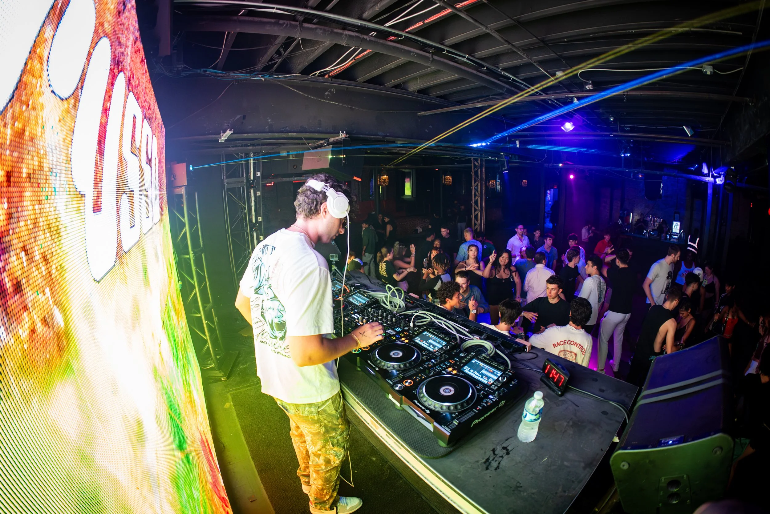 DJ performing at a nightclub with a crowd dancing and colorful lights.