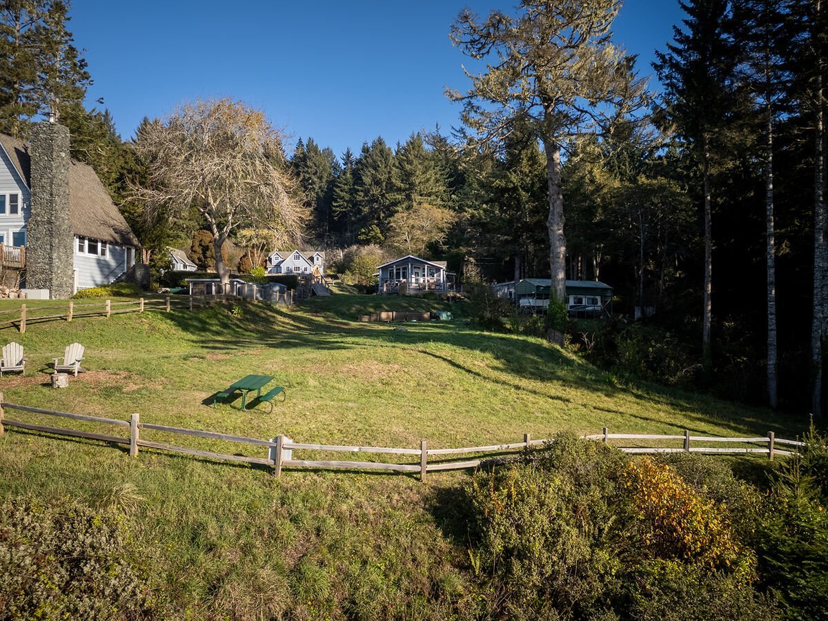 A grassy hillside with outdoor seating, trees, and houses in the background under a clear blue sky.